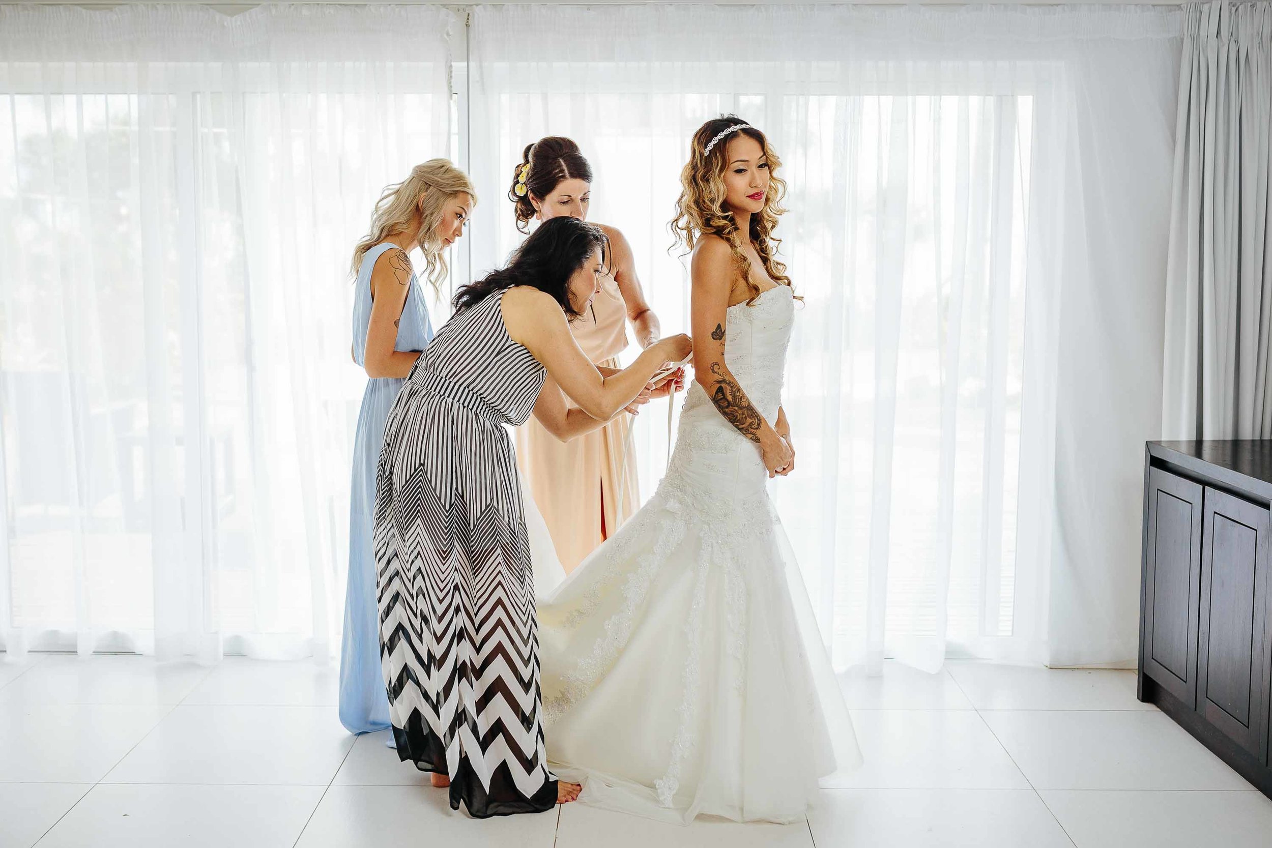 Mother of bride and friends helping bride with wedding dress