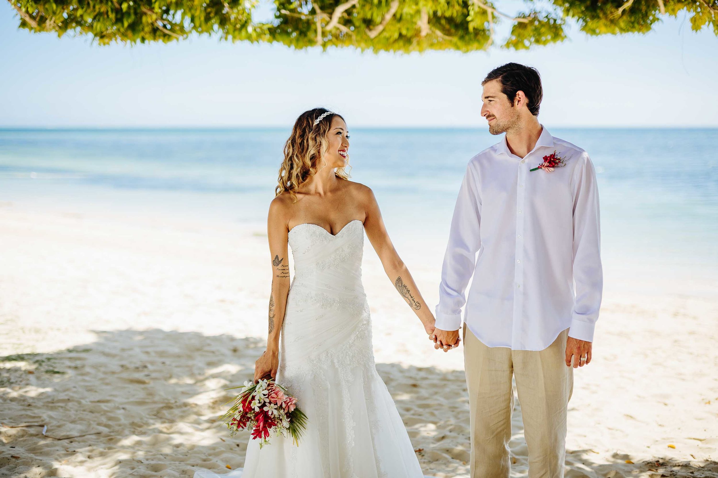 Bride and groom posing under a tree on the beach