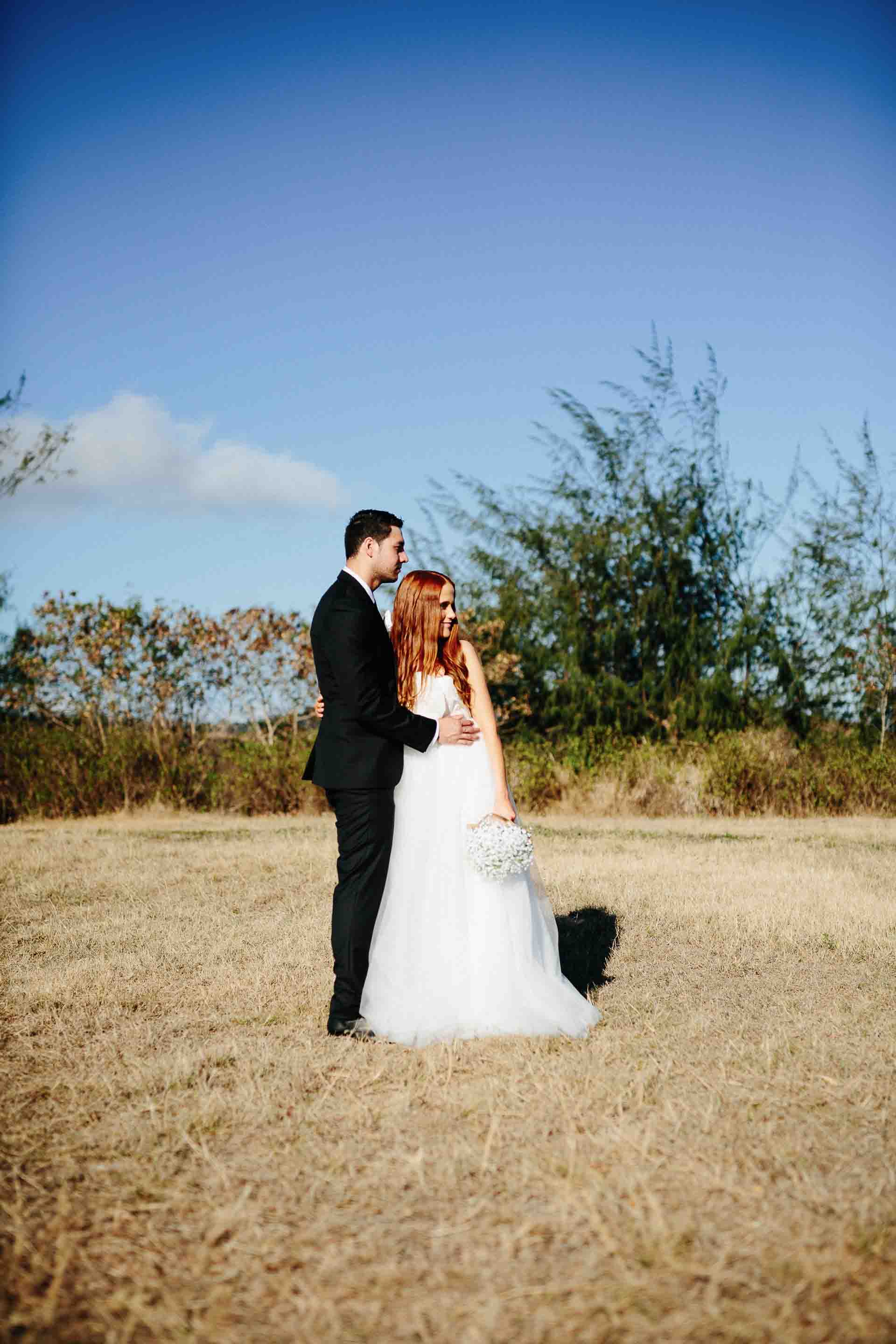 the newlyweds posing together in an open field with a blue sky behind them