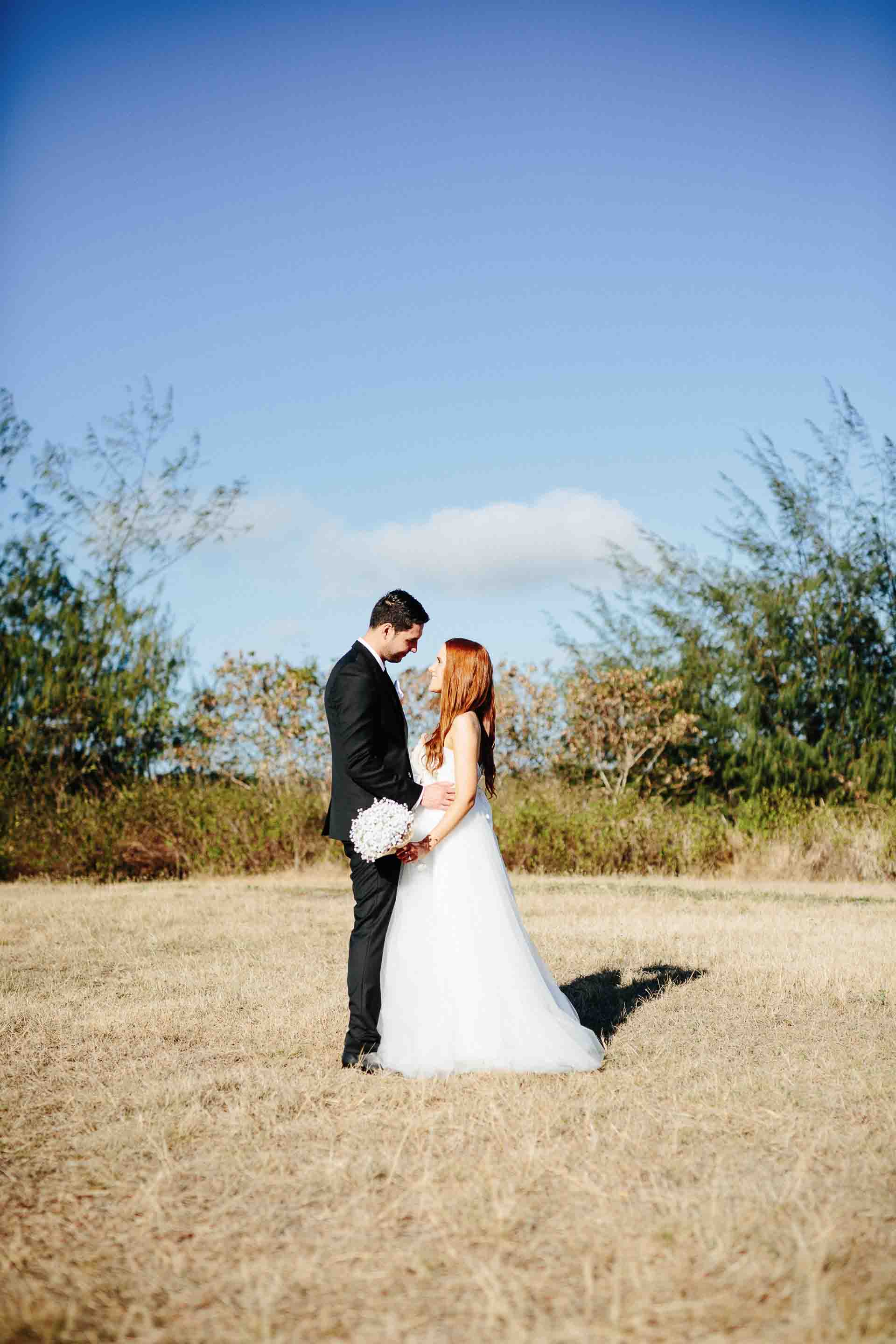 the couple sharing a moment together in an open field with a large field and blue sky behind them