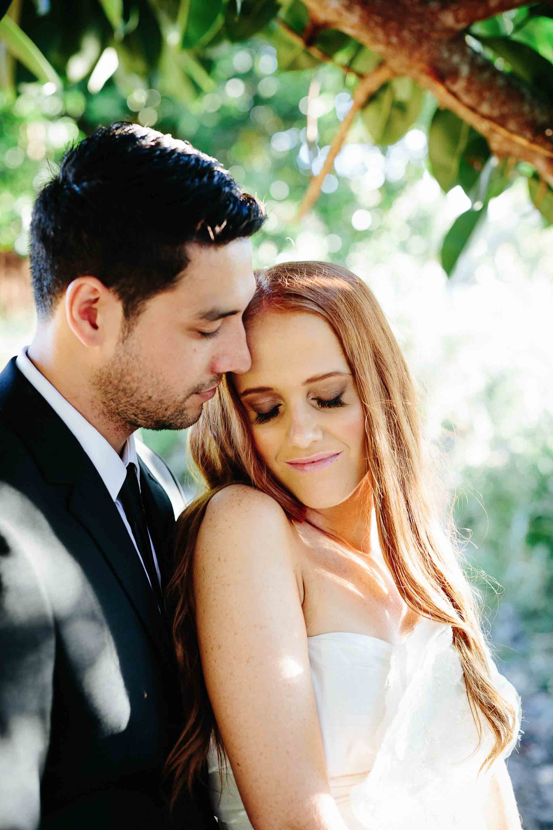 bride leaning against husband under the trees