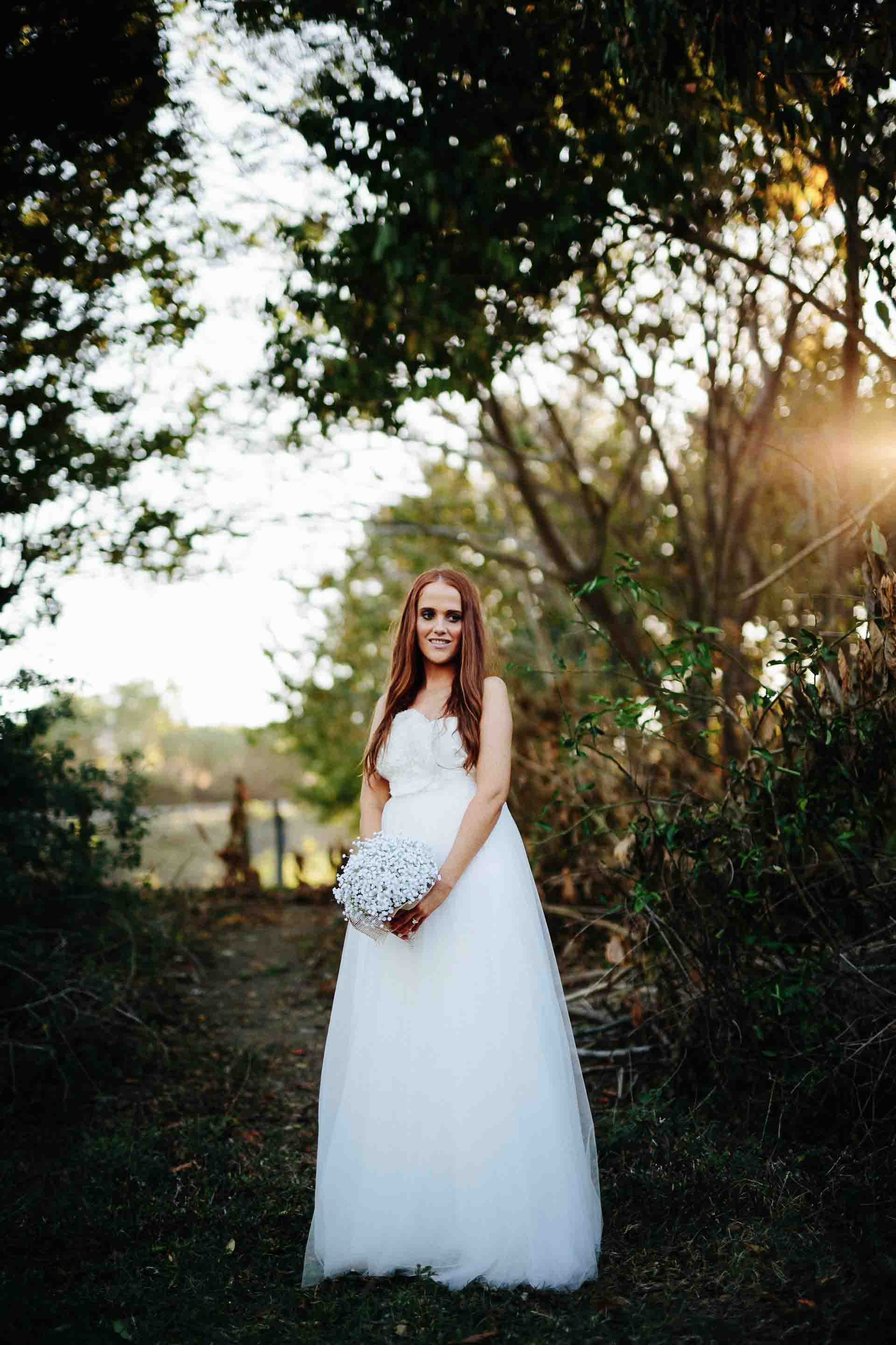 bride standing alone with sun behind trees in the background