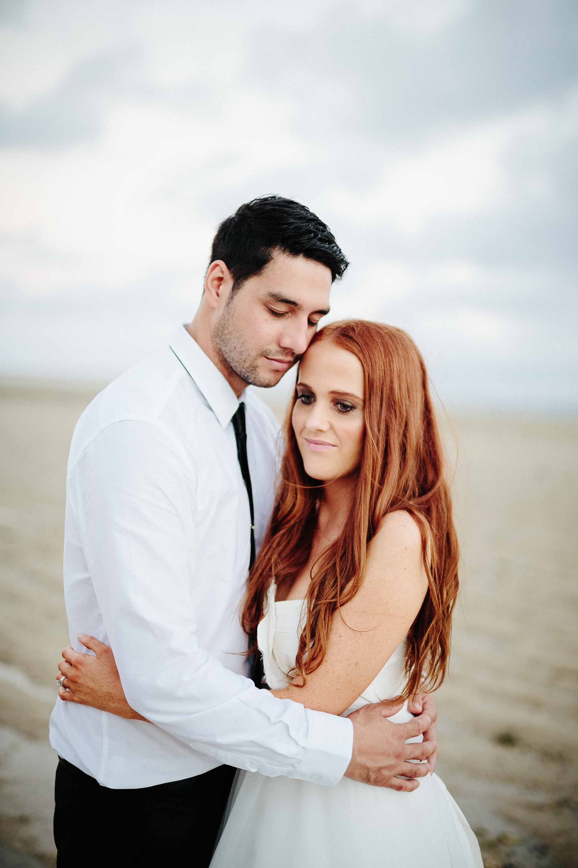 bride and groom holding each other gently on the the beach at sunset