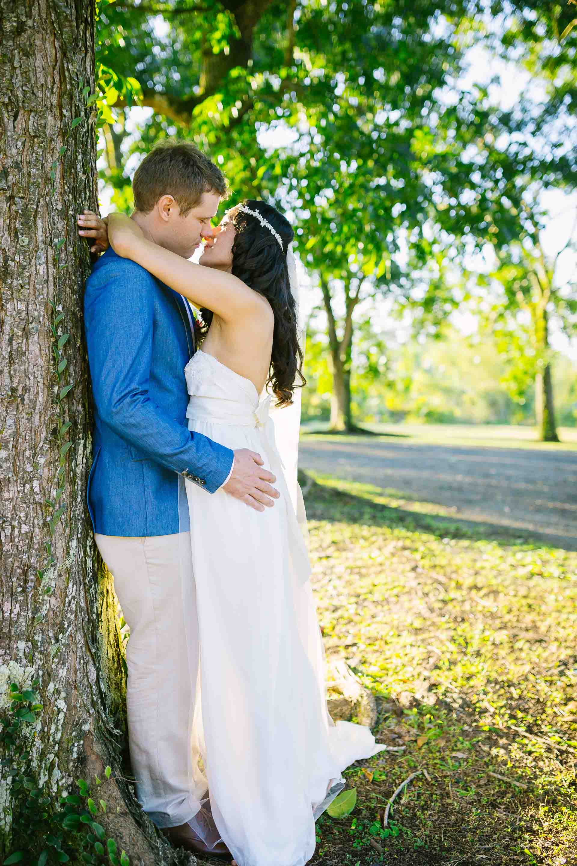 the couple kiss while leaning against a large tree