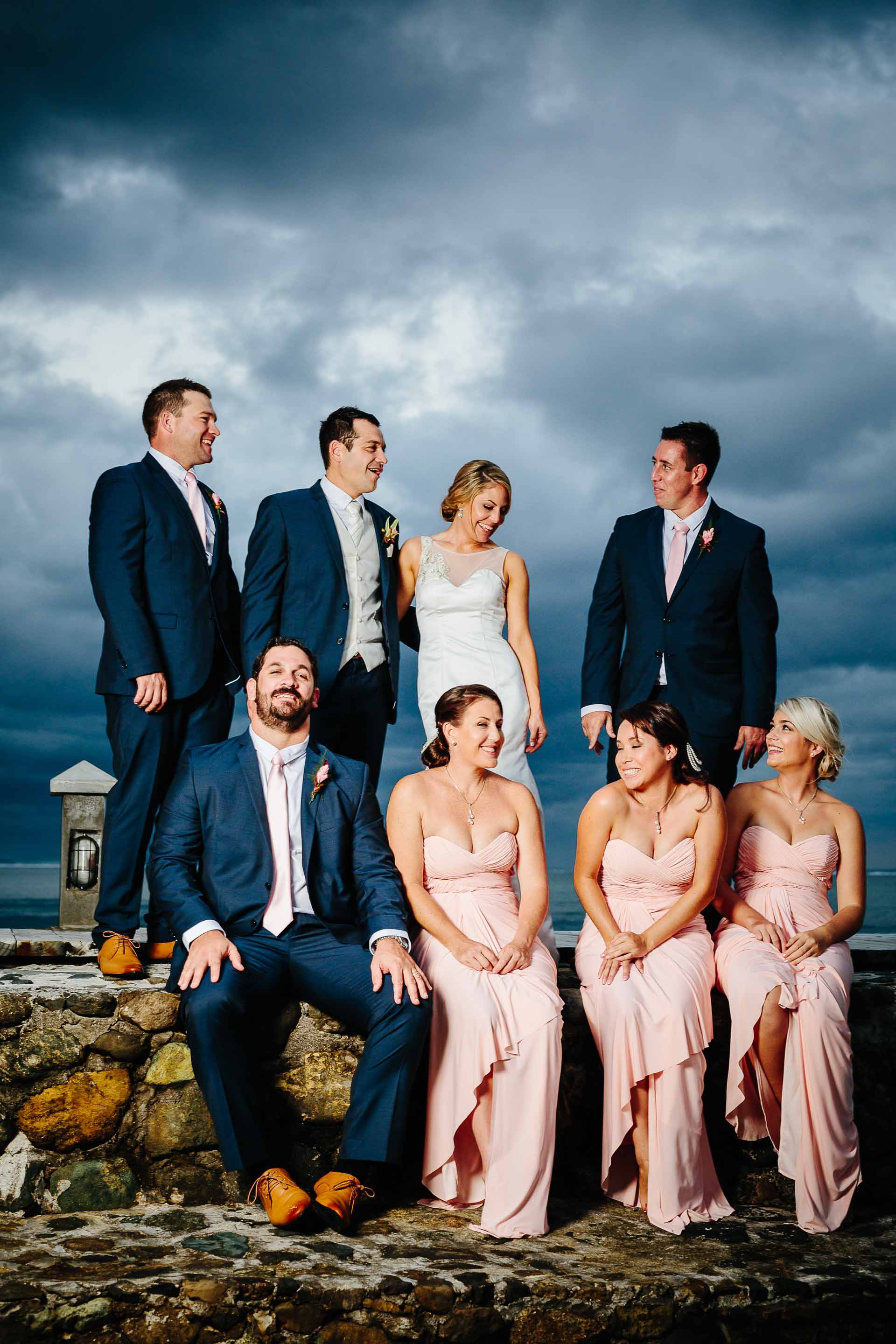 bridal party sitting on a pier with dramatic dark clouds behind them