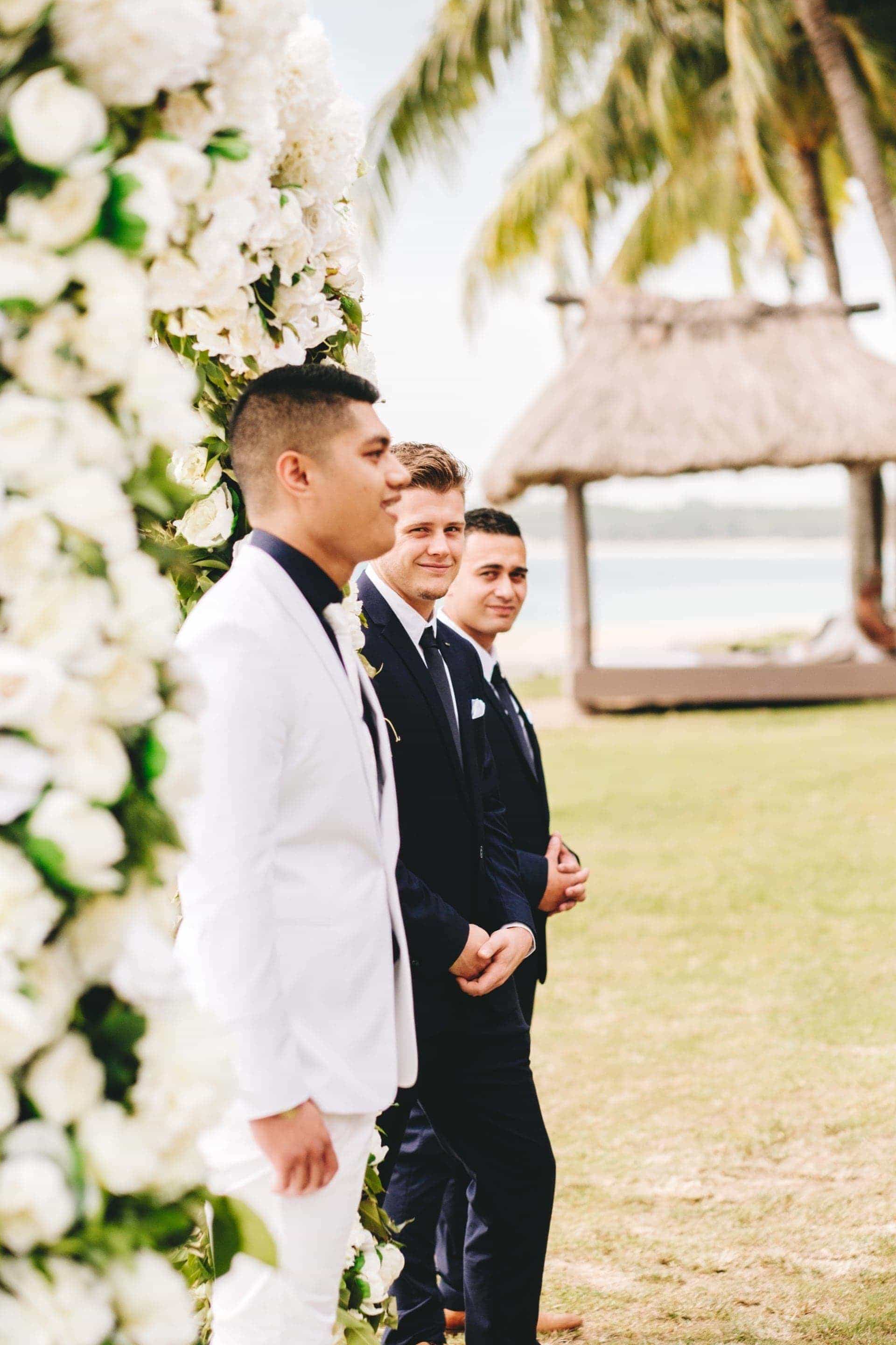 the groom waiting excitedly at ceremony arch as the groomsman and best man watch on