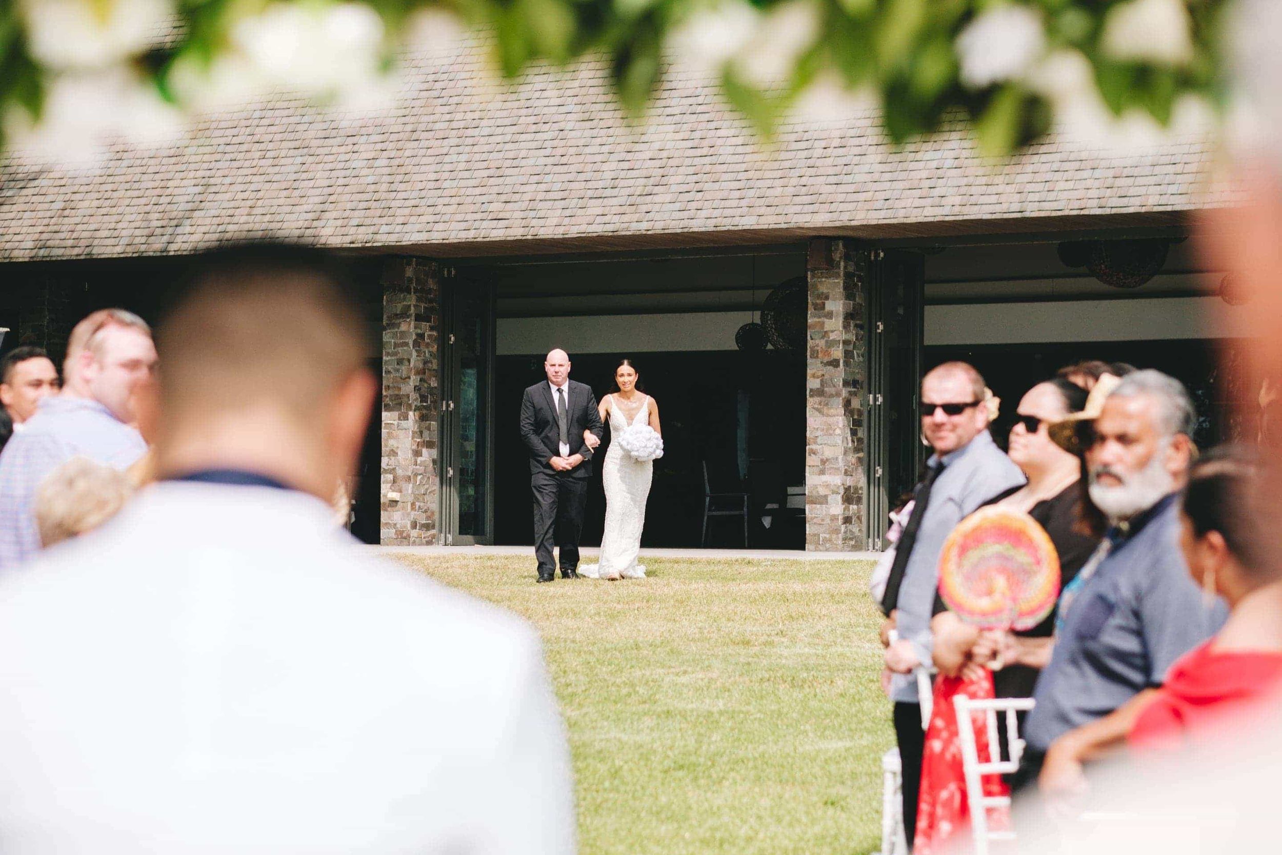 the bride and her father walking down the lawn aisle in front of the Navo Restaurant.