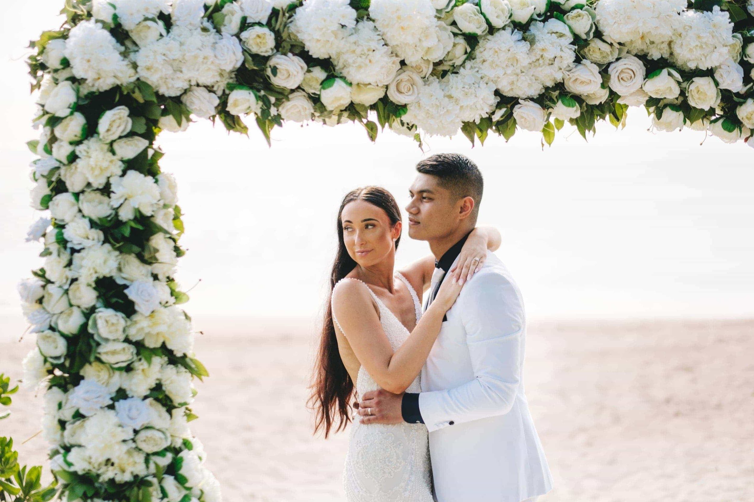 The newlyweds embrace under their white tropical wedding arch