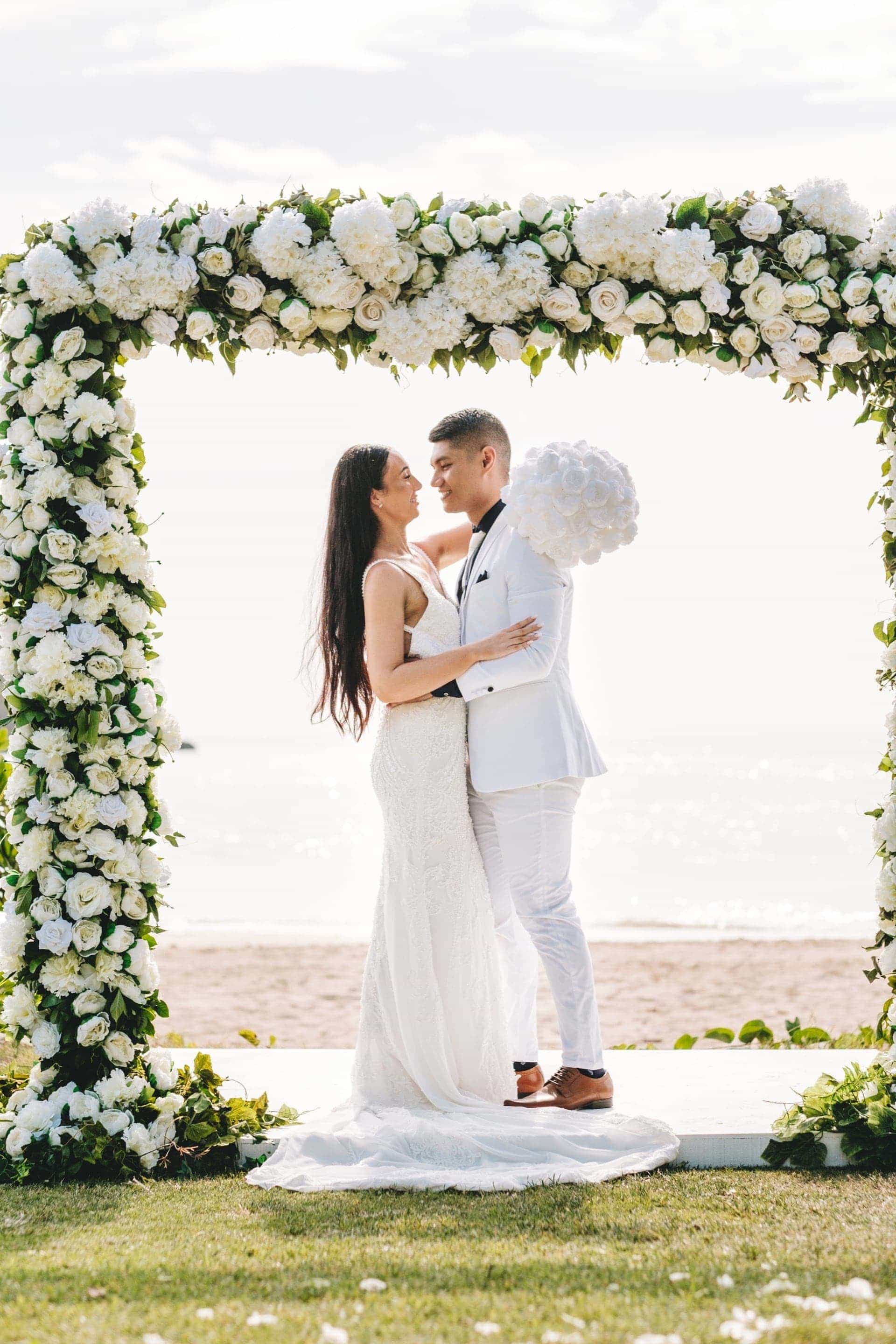 the bride embraces the groom under their wedding arch wither her beautiful bouquet in hand.