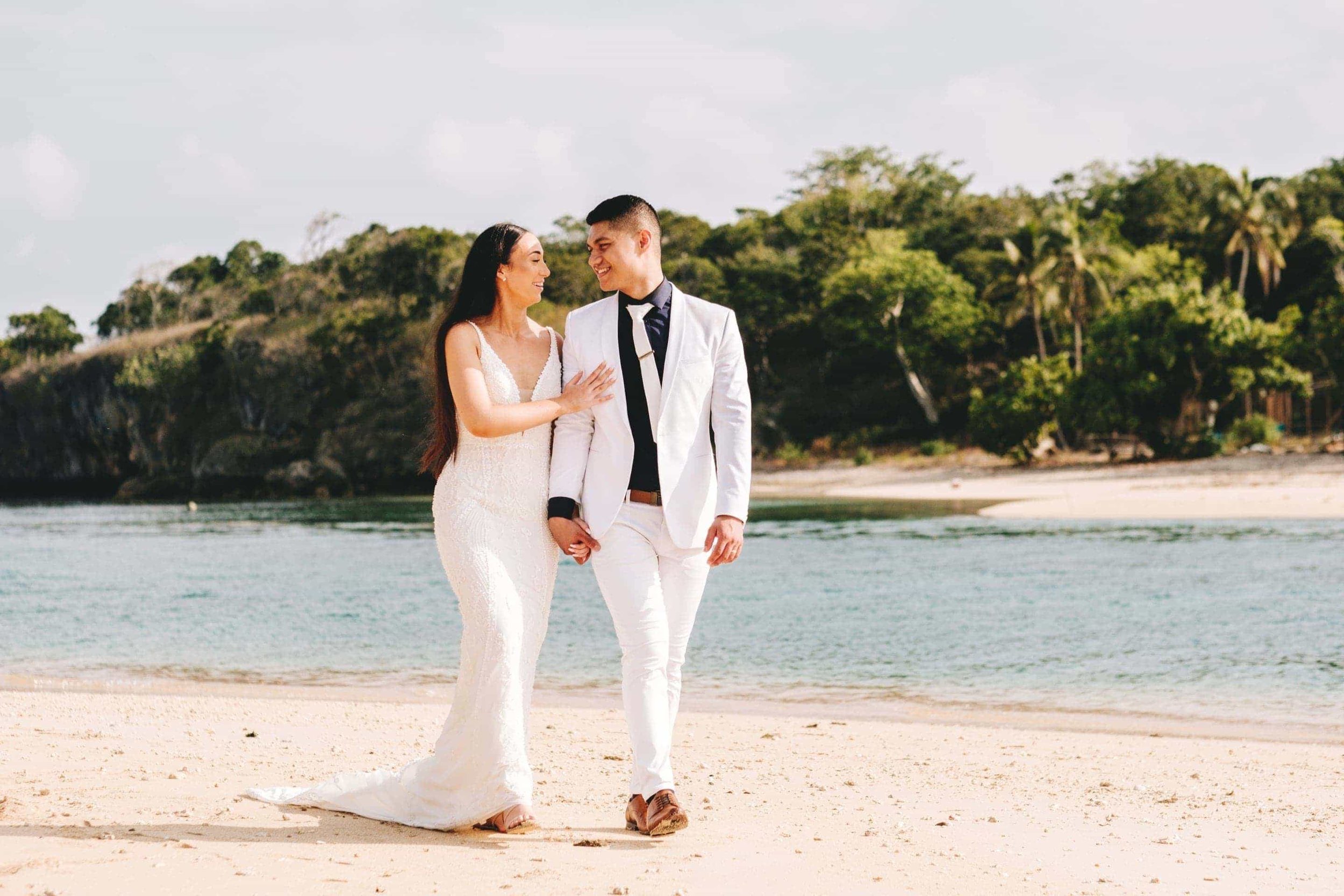 The bride and groom walking along the beautiful Natadola beach with the rugged Navo Island in the background.