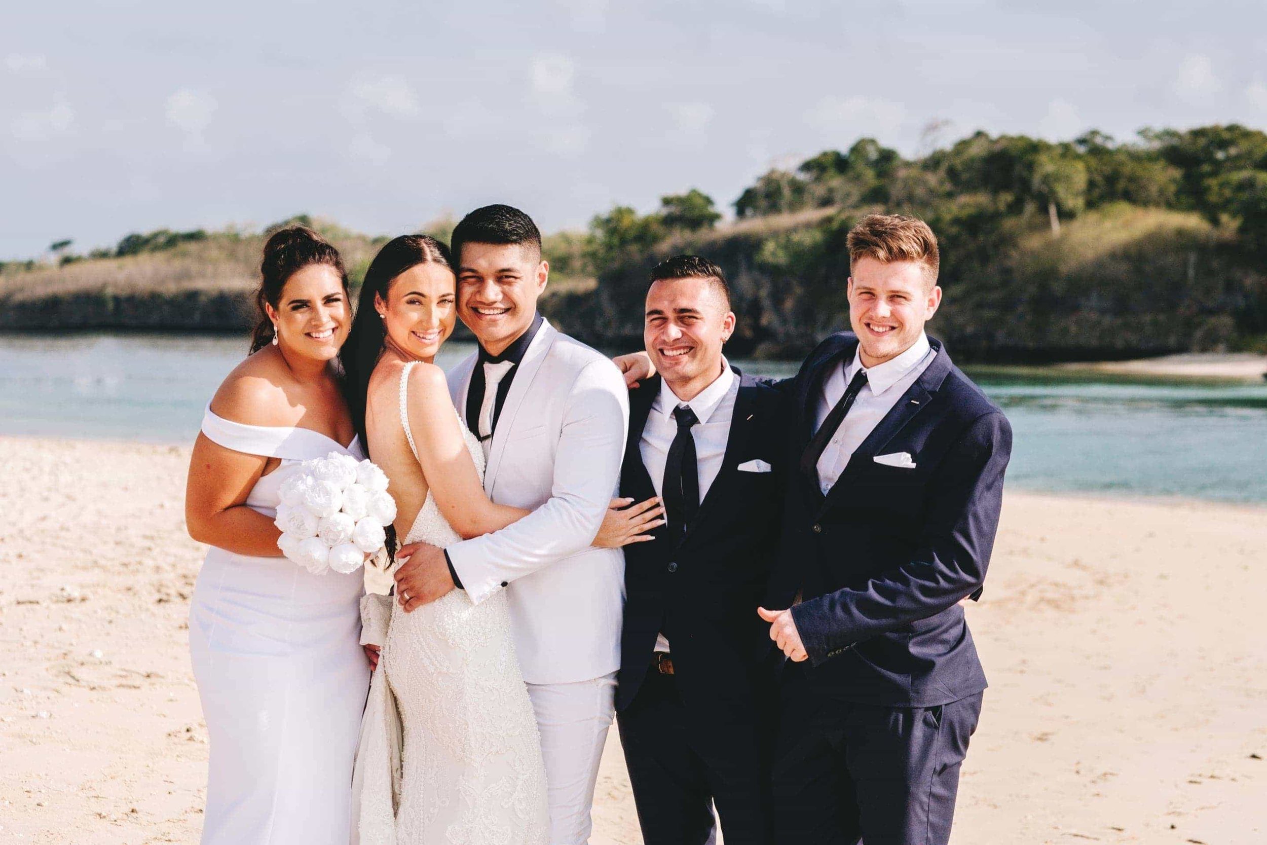 the bridal party embrace as they pose for a photo on Natadola beach with Navo Island in the background