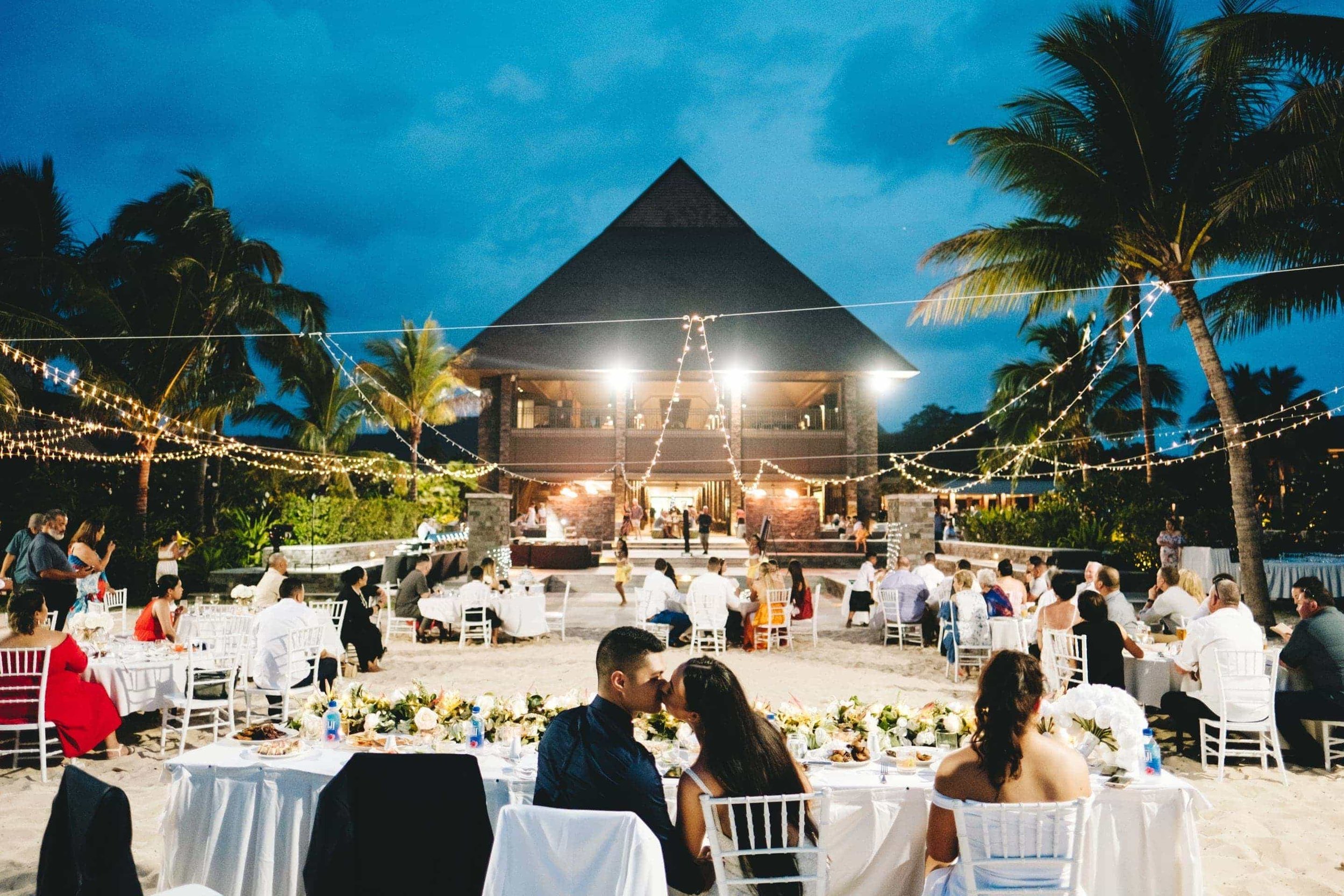 the couple kiss at their head table with the impressive main foyer and Kama Lounge bar before them