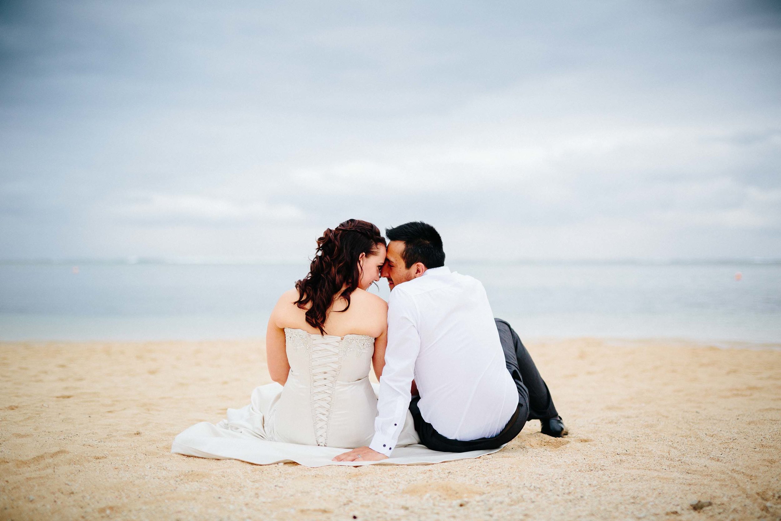 bride and groom sitting down on the beach kissing