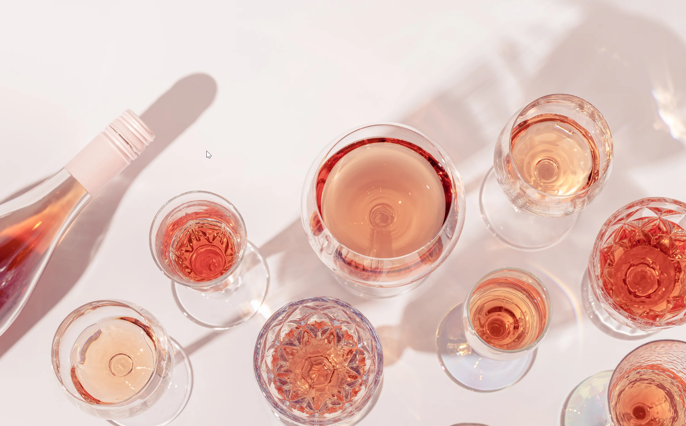 Flere glas med rosévin set fra oven, med skygger og reflekser på en lyse overflade.
