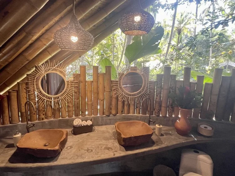 Bathroom with two wooden vessel sinks, bamboo wall decor, and tropical plants in a rustic, natural setting.