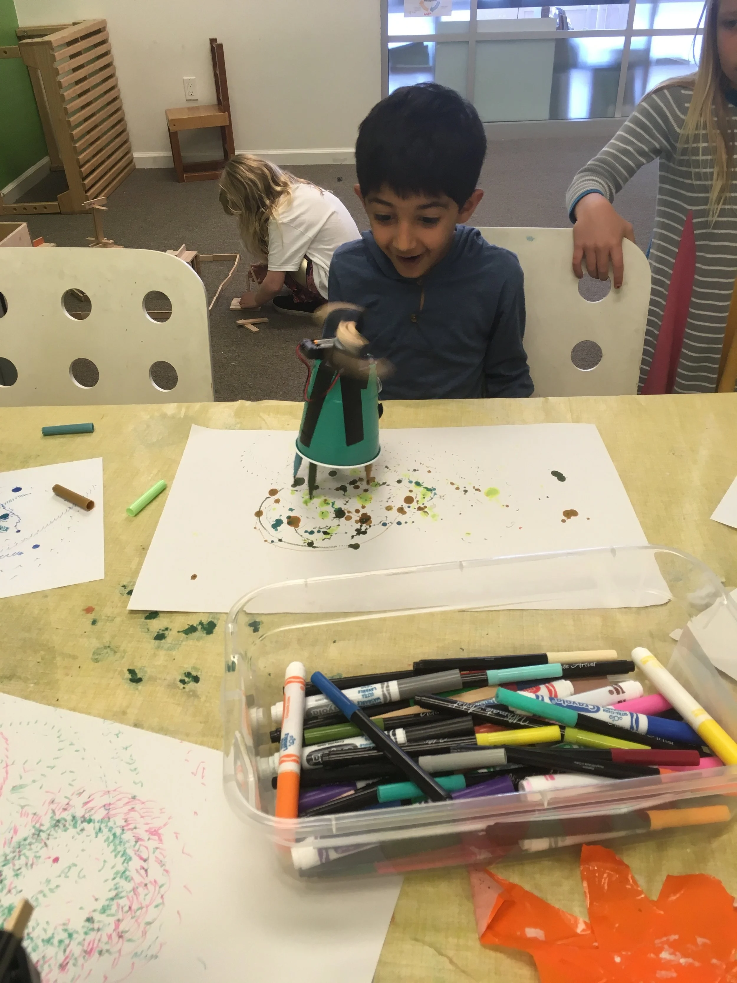 Student excitedly watching a robot create colorful art with markers.