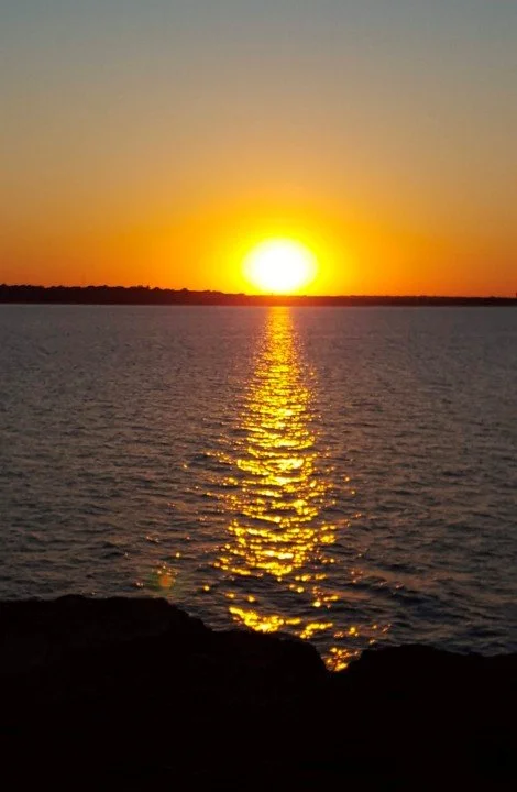 An orange sunset over the water and distant land.