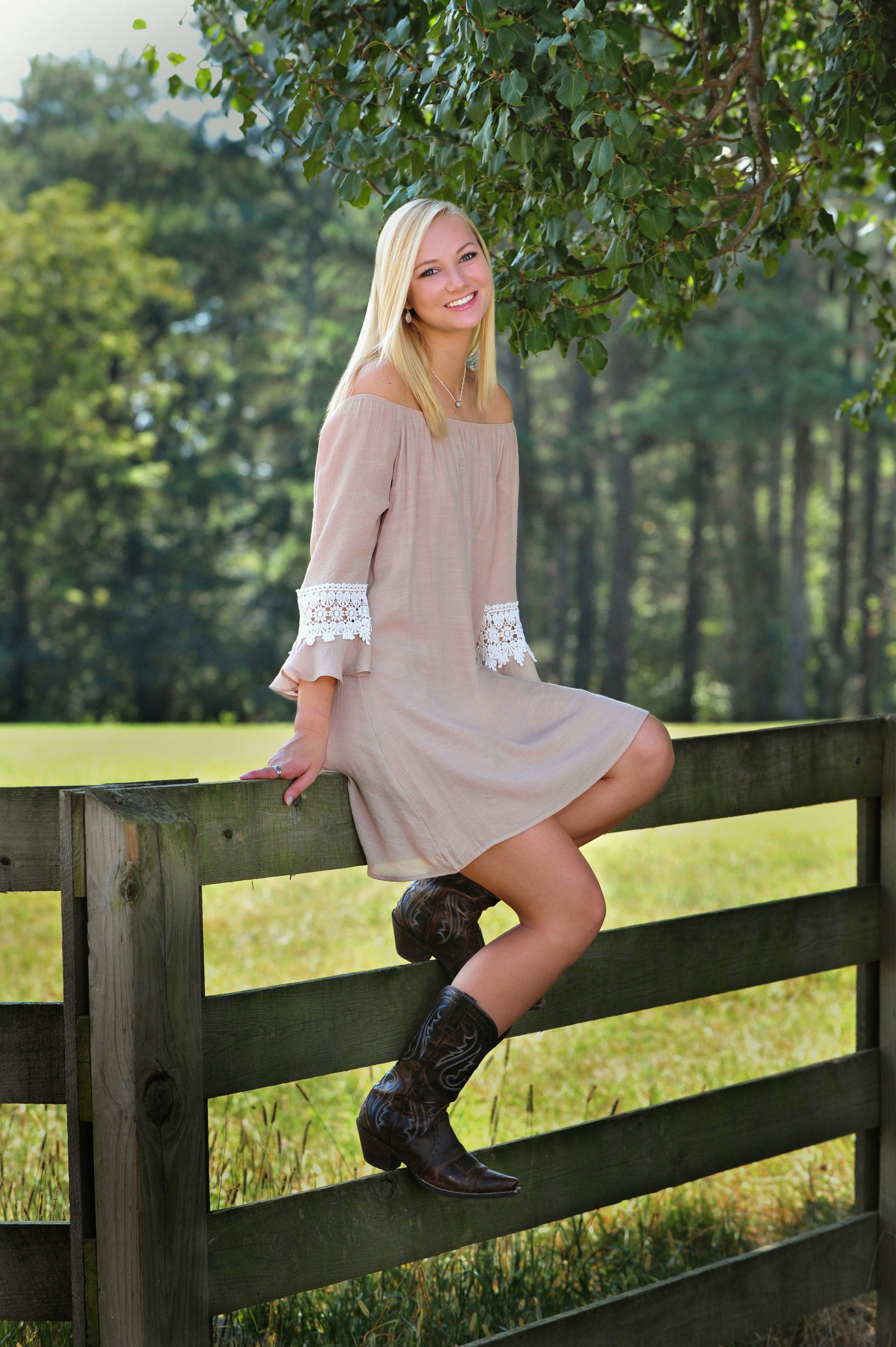 Senior portraits girl sitting on fence in cowboy boots outside