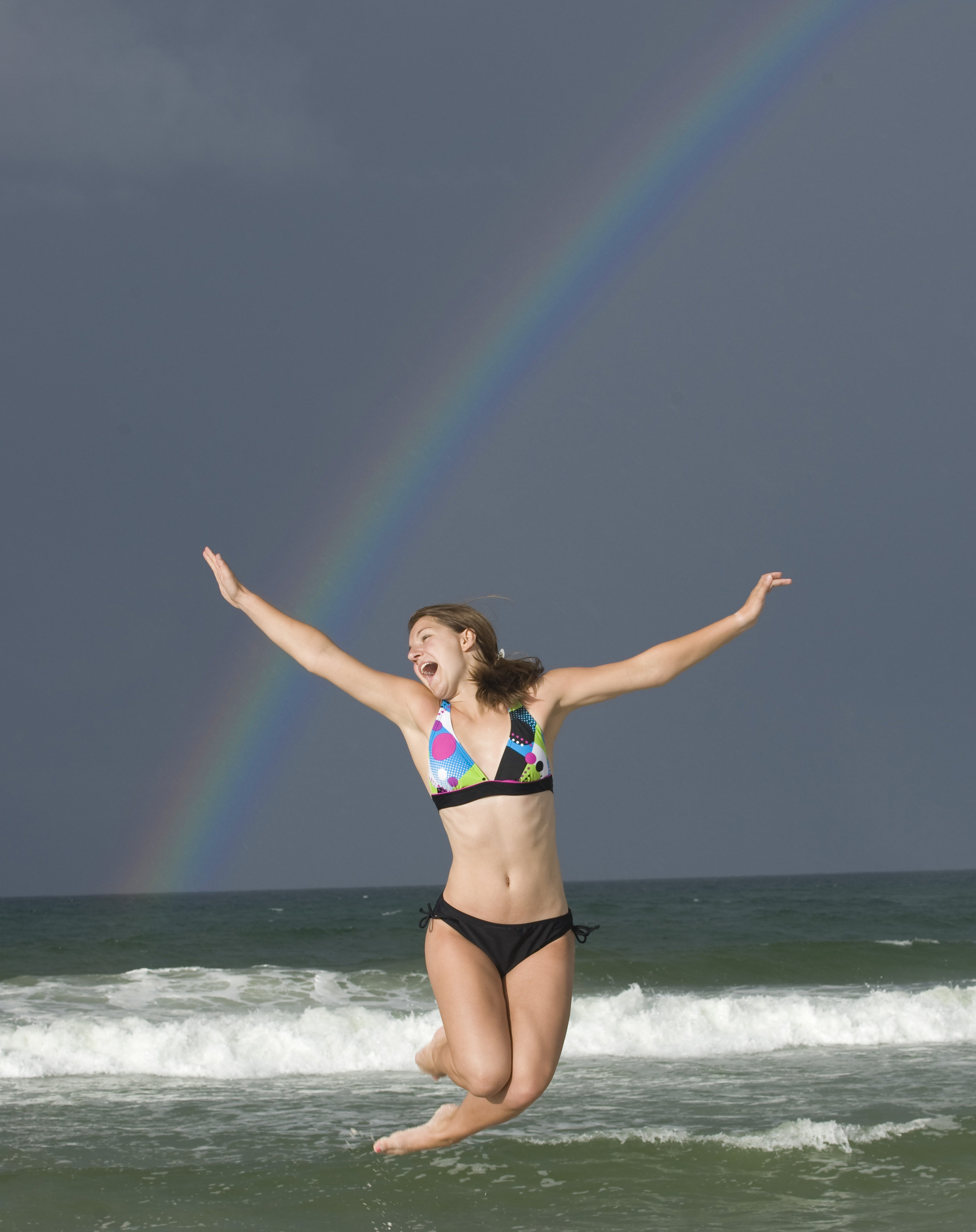 senior portrait girl at beach jumping in front of rainbow