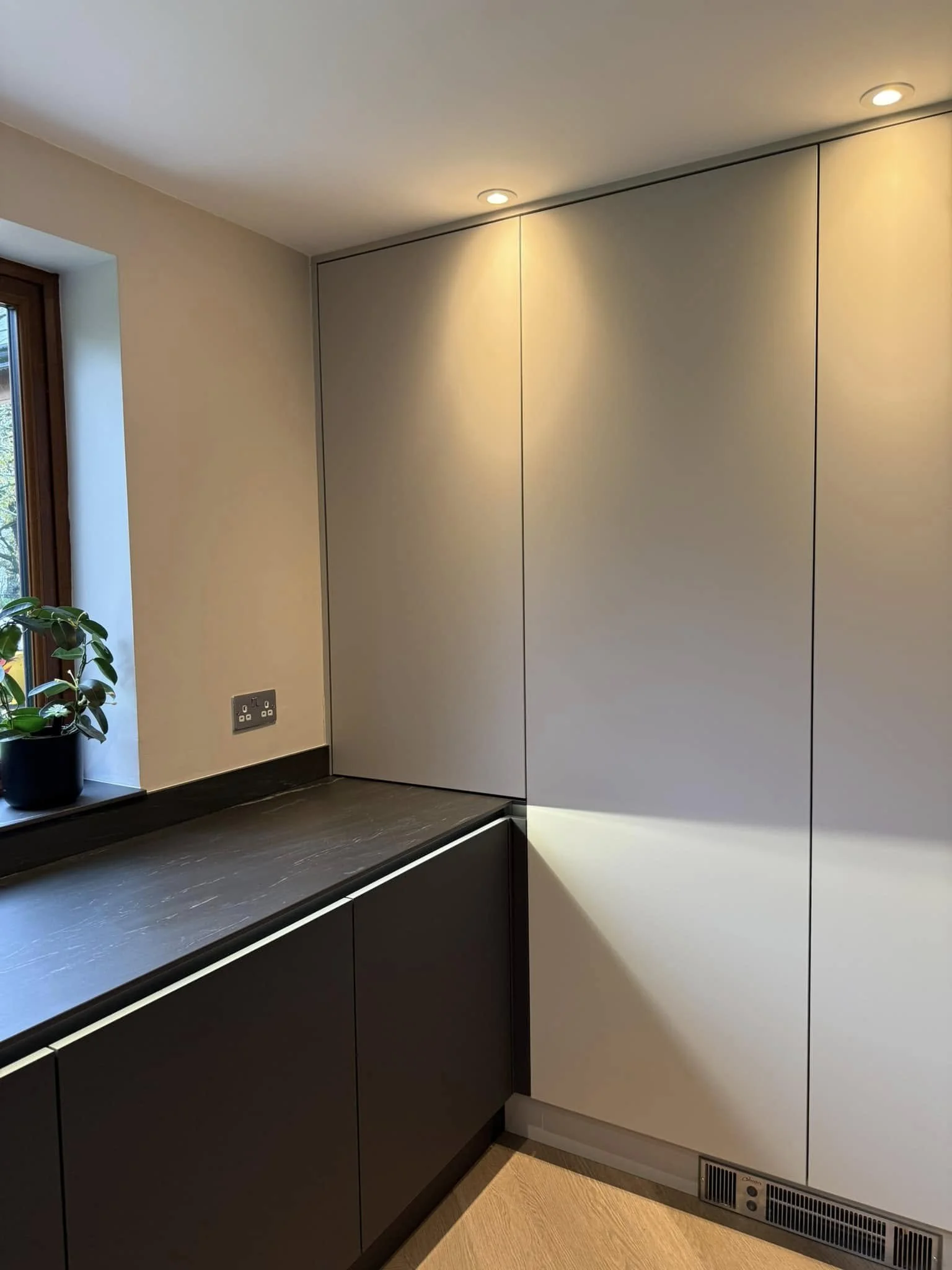 Closed tall unit cabinet beside window run with black quartz worktops and handleless base units in a modern kitchen..jpg