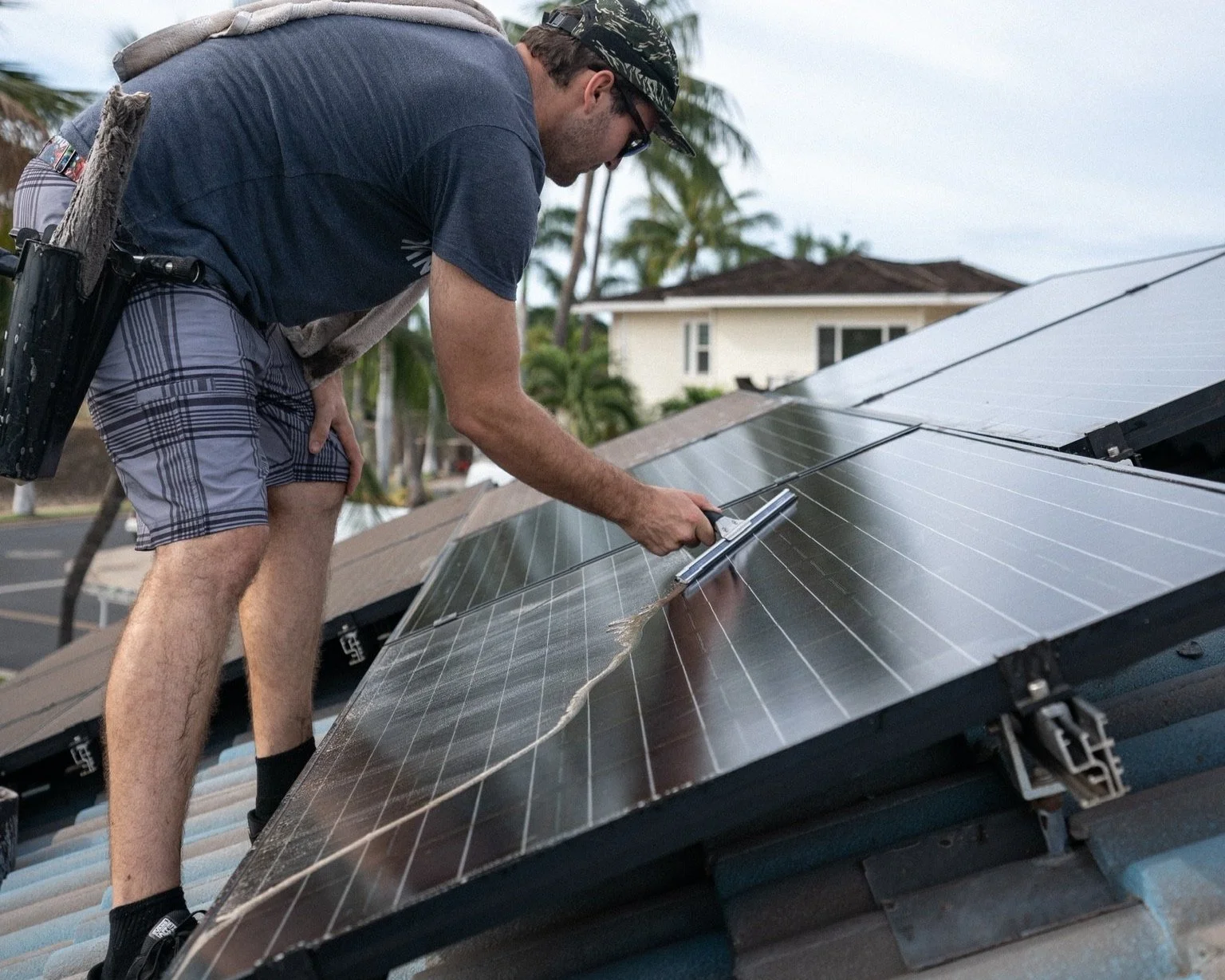 Technician squeegeeing rooftop solar panels on a tile roof, palm trees behind