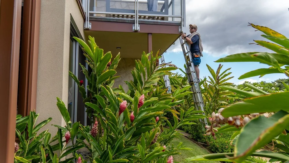 Window cleaner on a ladder cleaning upper-floor glass railings at a Kaanapali home