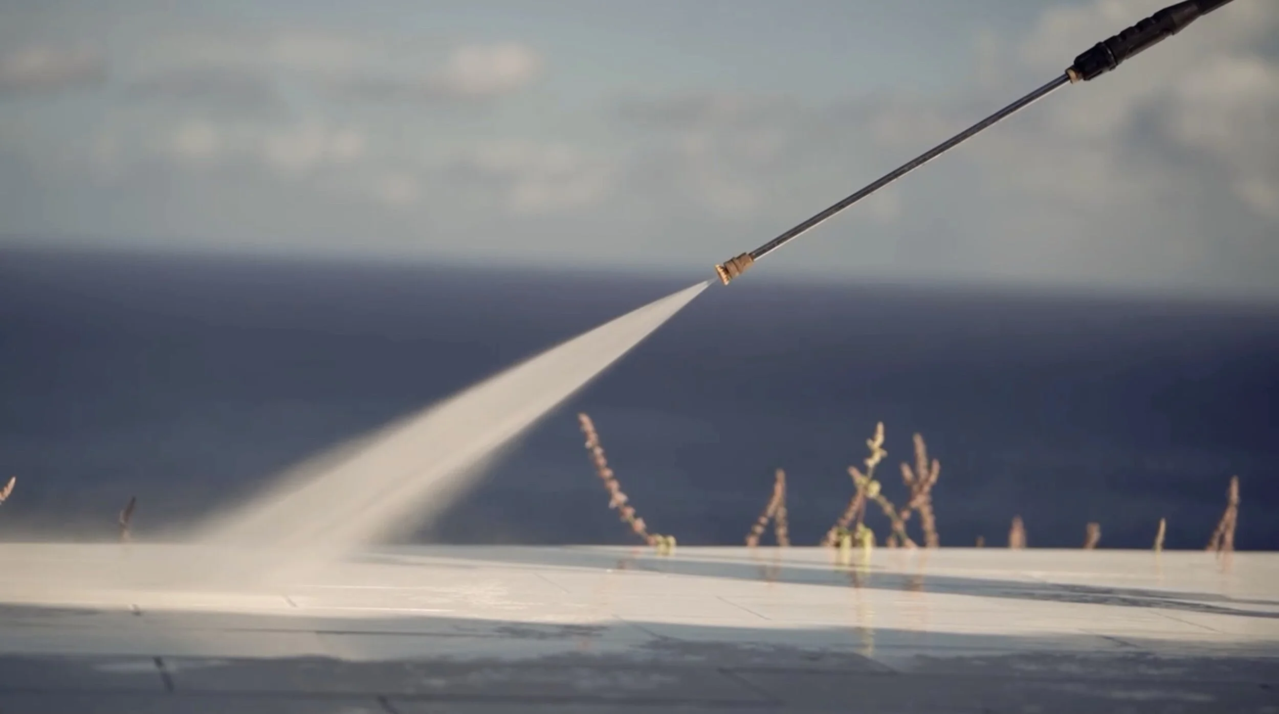 Pressure washer wand spraying a white deck with the ocean in the background