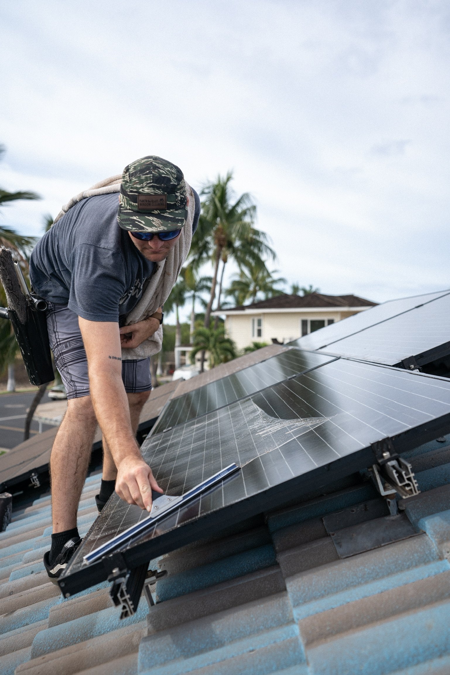 Window cleaner squeegeeing solar panels on a tile roof with palm trees and a house behind