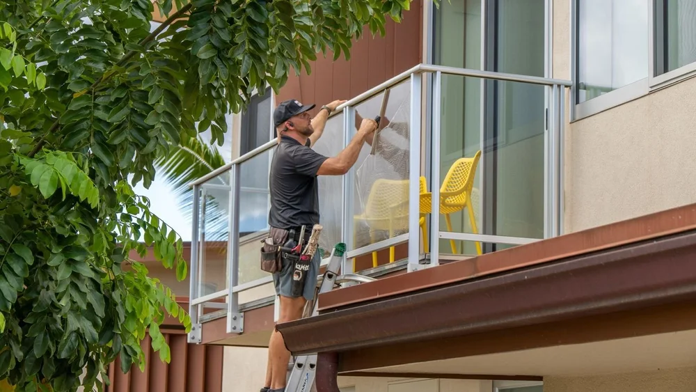 Window cleaner on a ladder cleaning glass balcony railings in Kihei