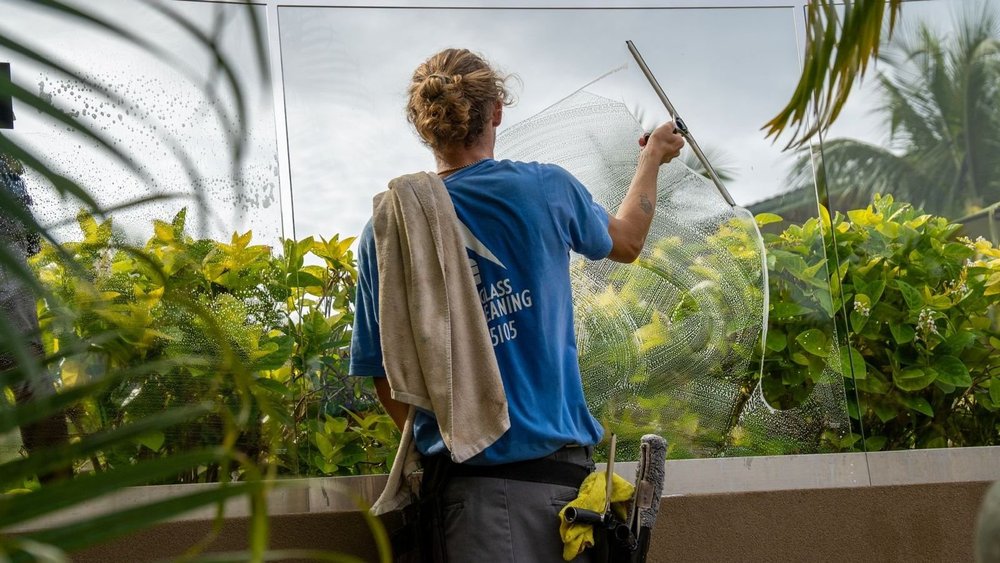 Window cleaner squeegeeing a glass railing at a Maui home