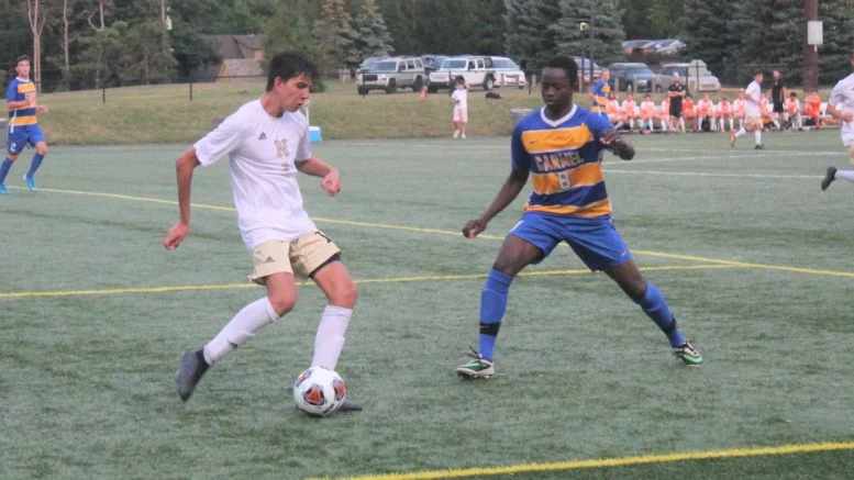 Noblesville's Owen Mejia (left) prepares to kick the ball as Carmel's Babacar Diatta plays defense during the Greyhounds-Millers boys soccer game Thursday at Carmel's Brian Murray Stadium. The game, which was the season opener for both teams, ended in a 1-1 tie. (Richie Hall)