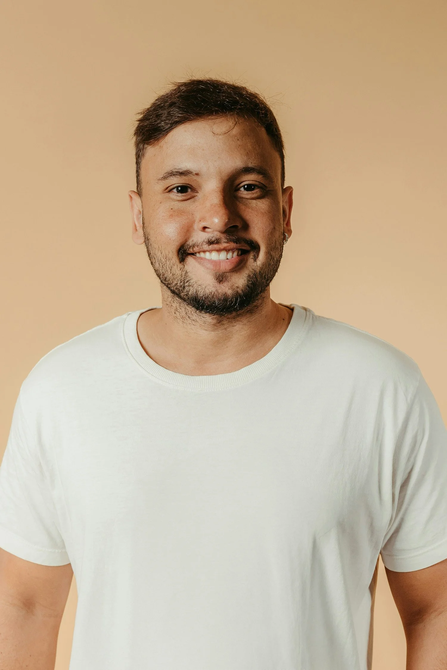 A person in a white shirt smiles before an orange-tan background