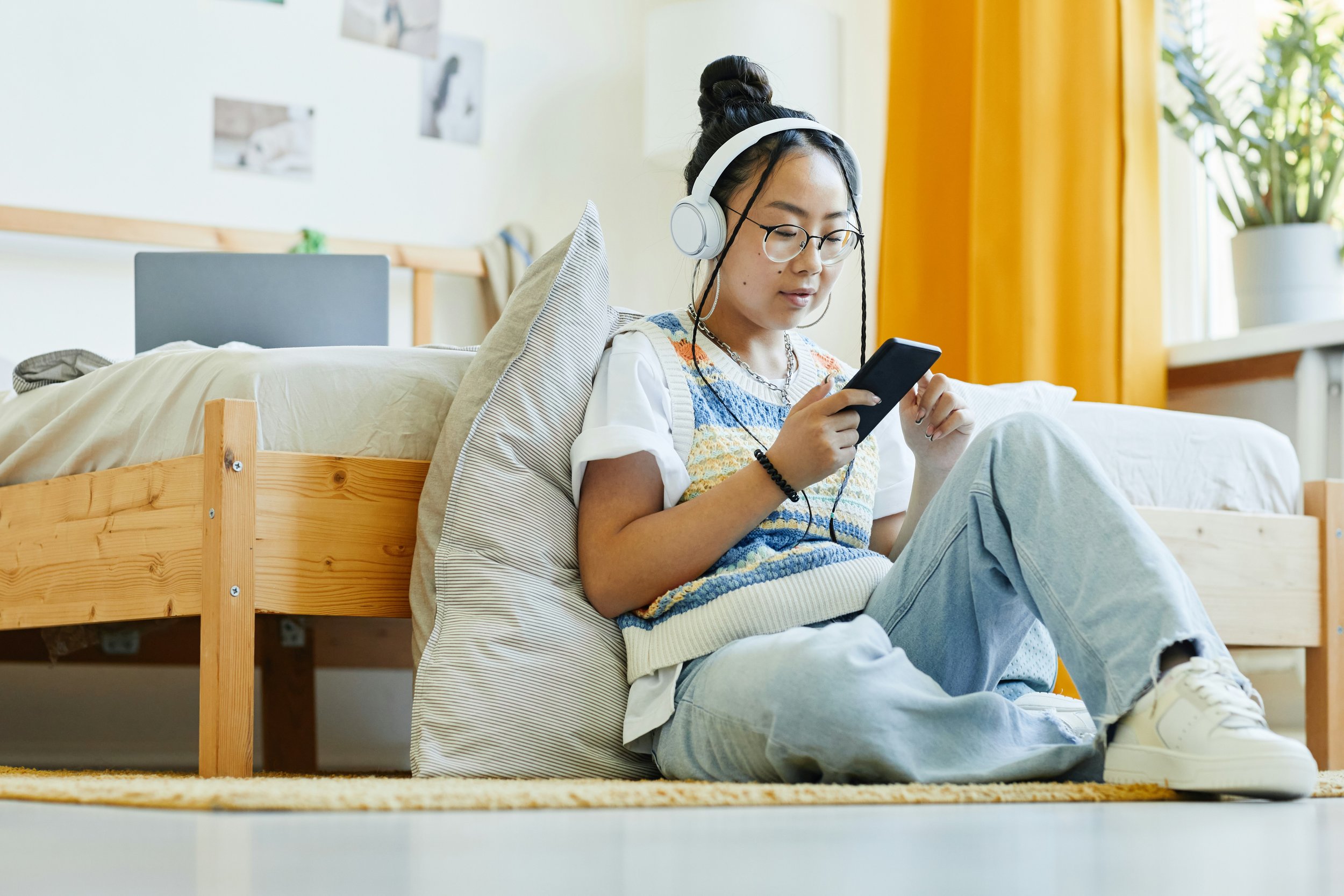 A teenager sits on their bed, scrolling on their phone