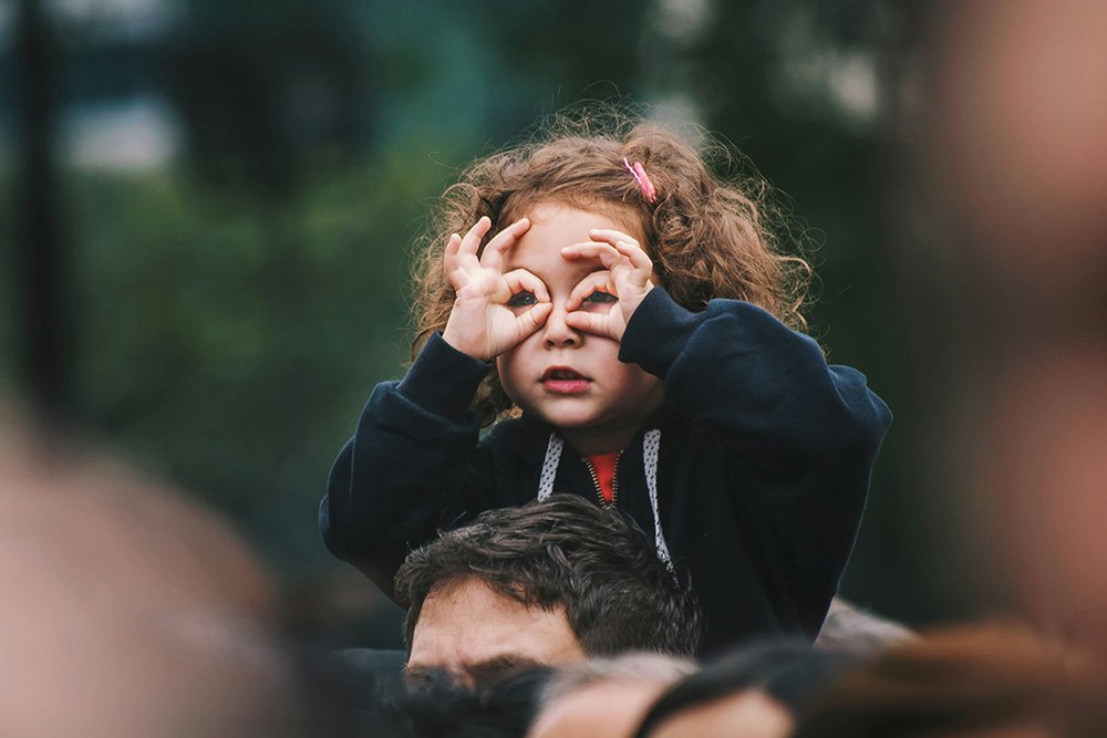 A child sits on their parent's shoulders, fingers lining their eyes