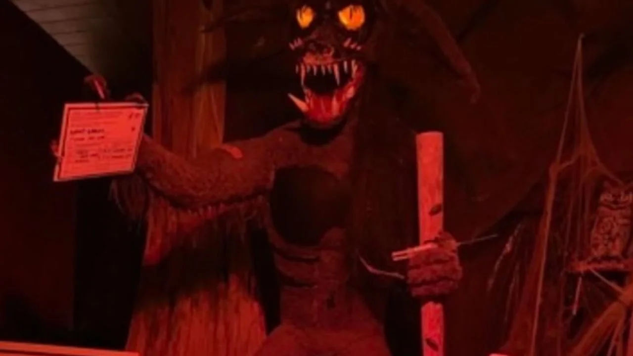 A snarling Rougarou figure holding a wooden staff in a red-lit haunted display.