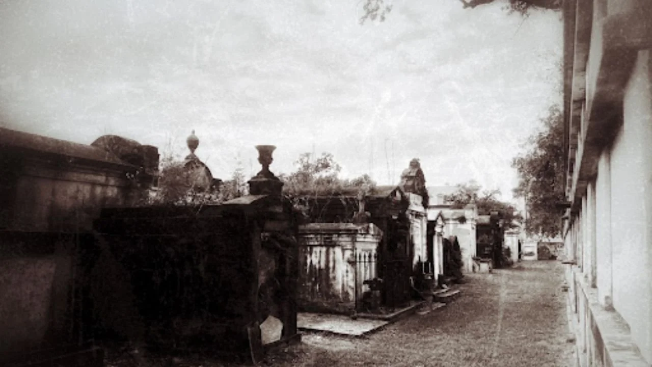 A sepia-toned photograph of a serene cemetery, featuring weathered gravestones and scattered autumn leaves.  