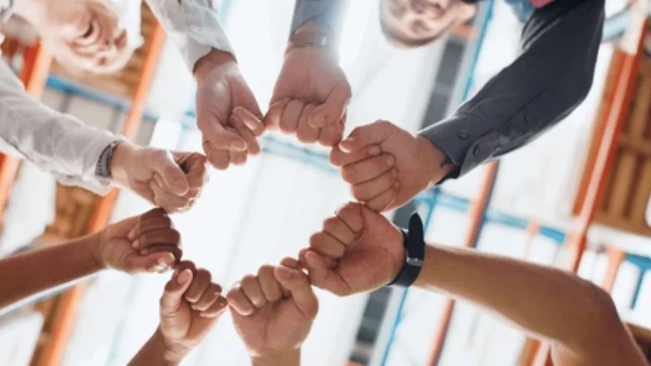 A diverse group of employees standing in a circle, holding hands, symbolizing unity and togetherness. 