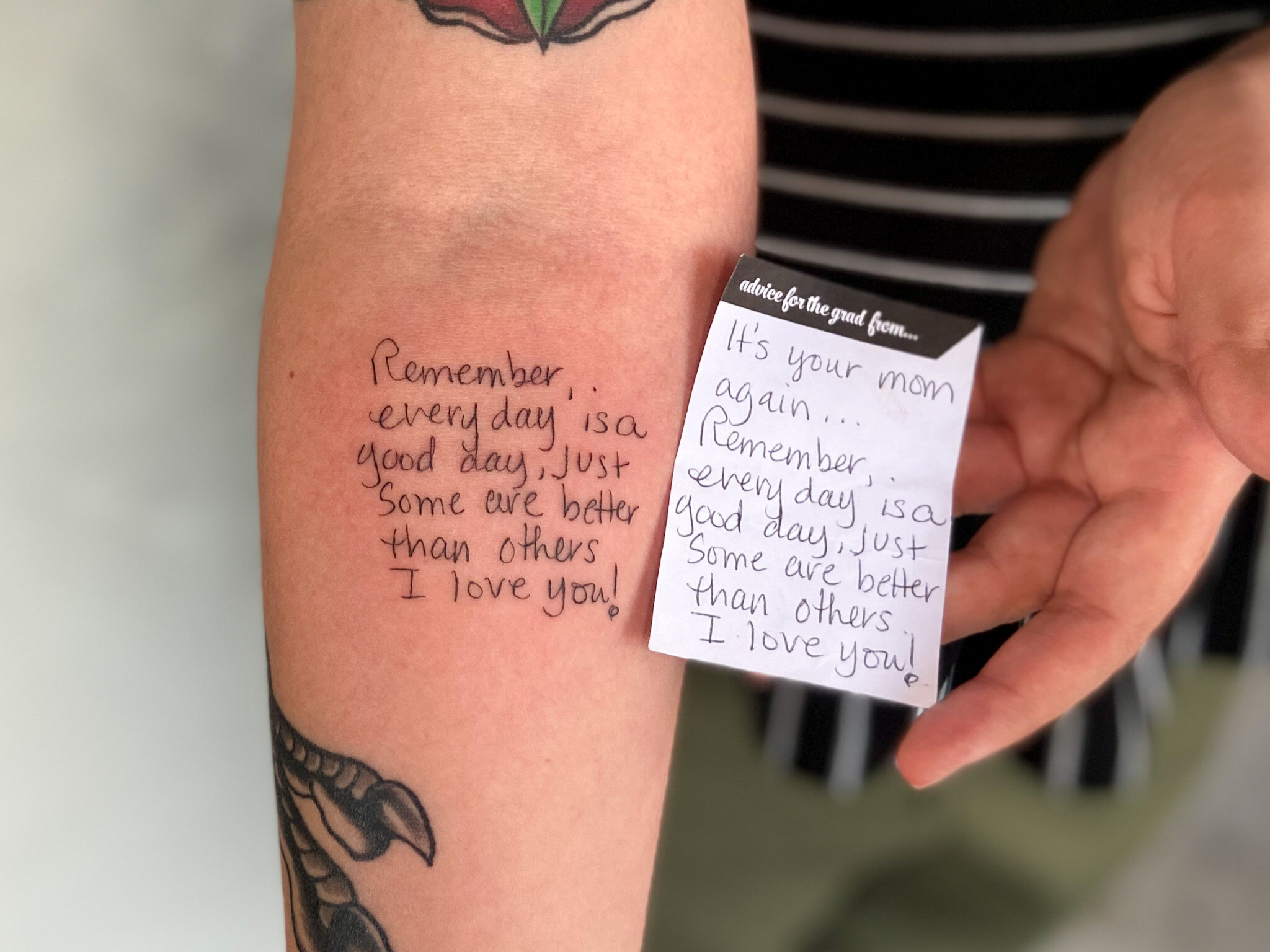  tattoo of a handwritten note by their mom. note is written on a sticky note paper and held next to the tattoo of the handwriting on a forearm with beige skin tone.   