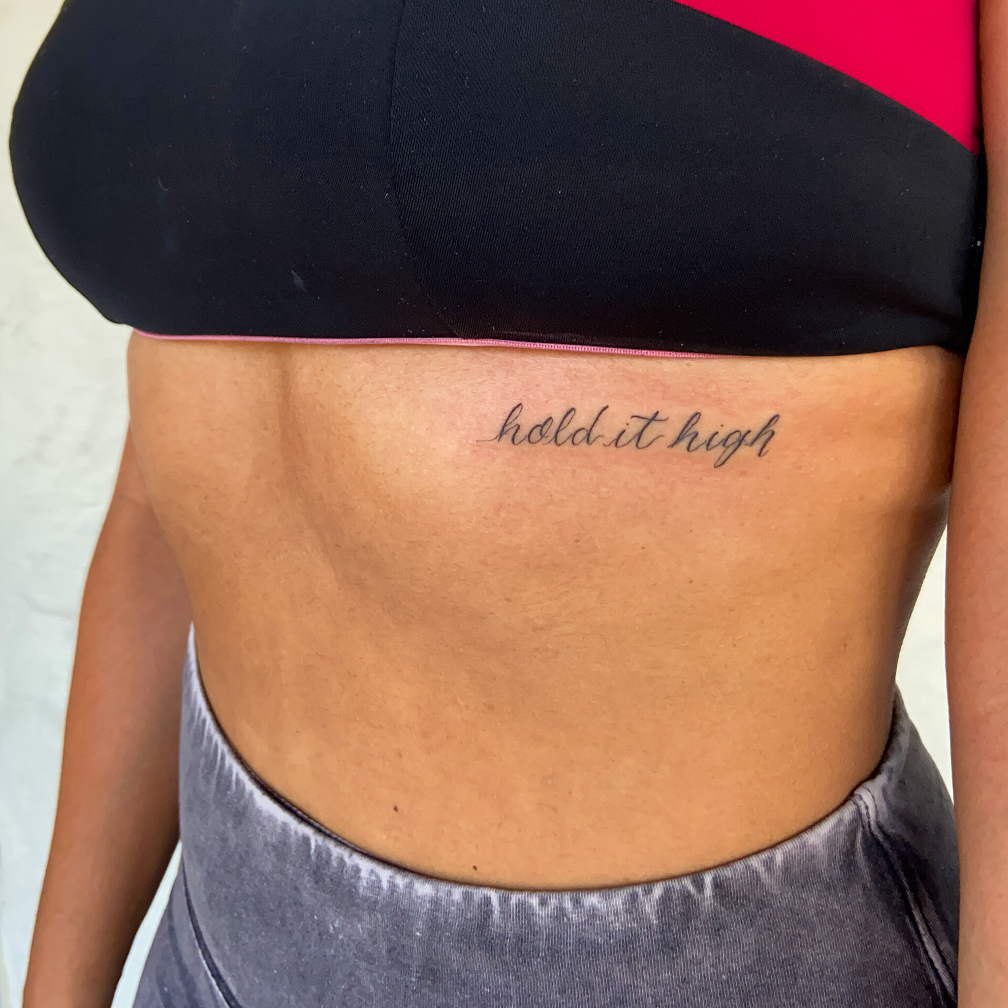  small script tattoo that says "hold it high" along a woman's ribcage 