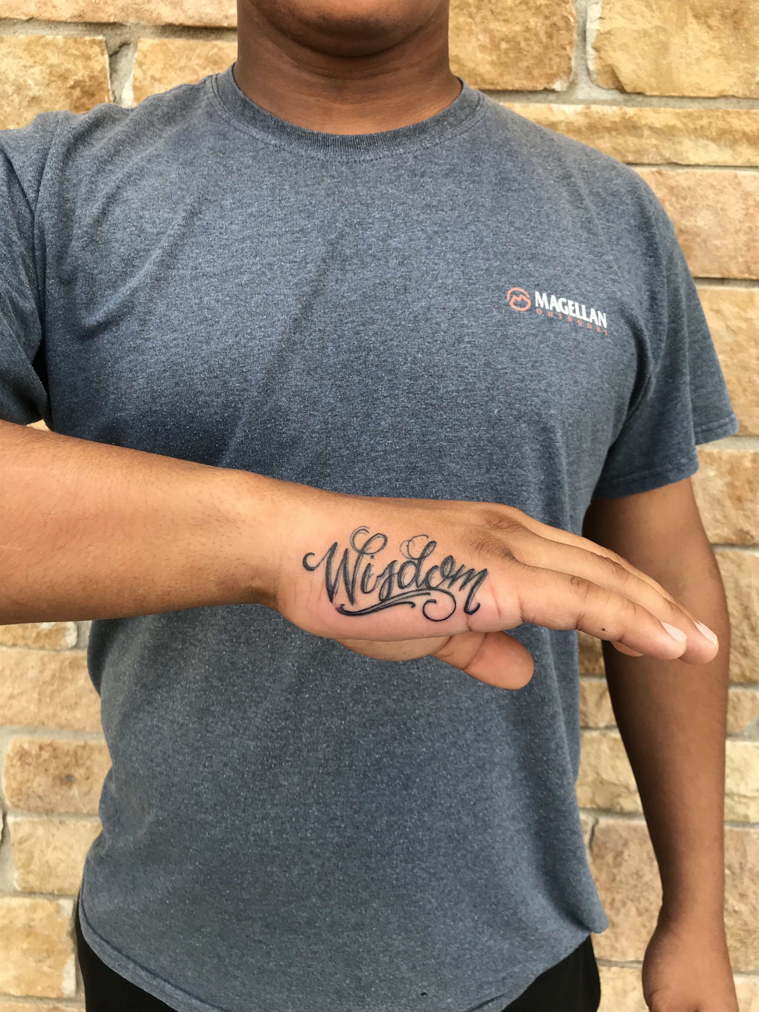 "Wisdom" in script lettering on the side of a hand. 