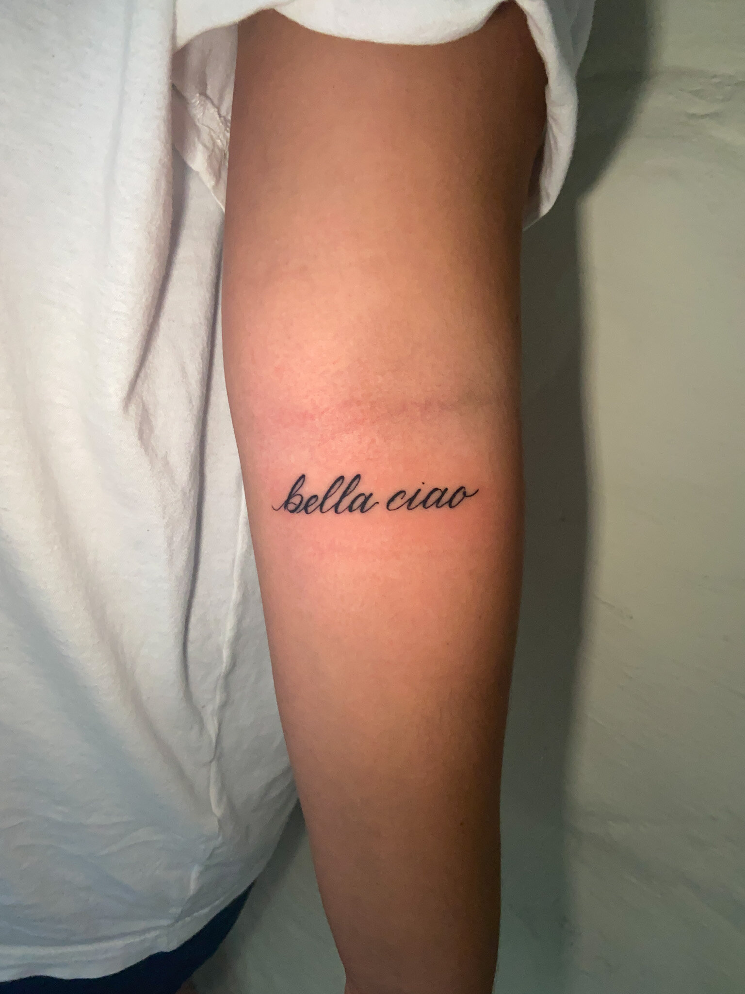  script lettering tattoo of the words “bella ciao” on a forearm 