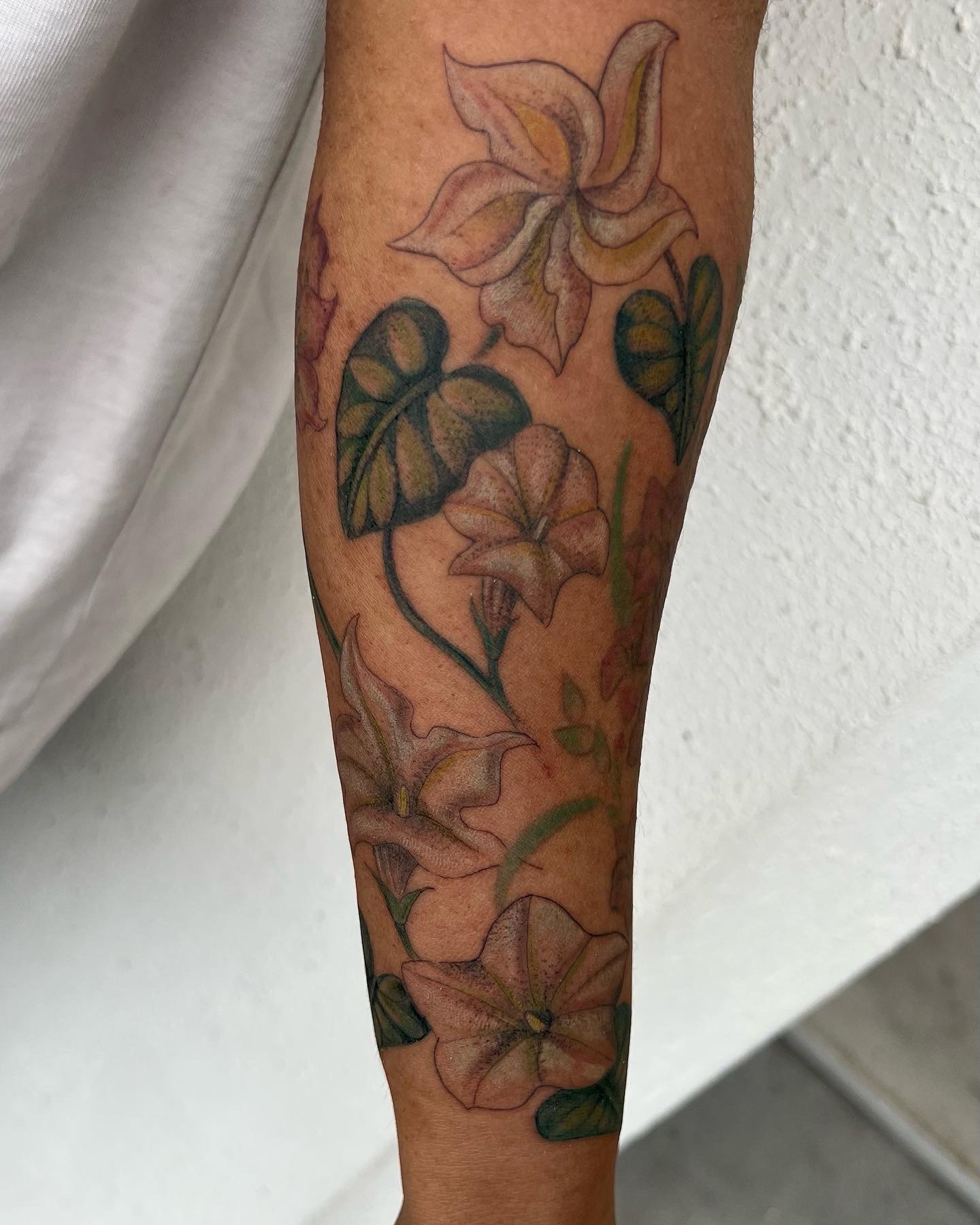  color tattoo of vining flowers on highly melanated skin. The green looks vibrant and beautiful with illustrated flowers on dark skin, forearm of woman. half sleeve  