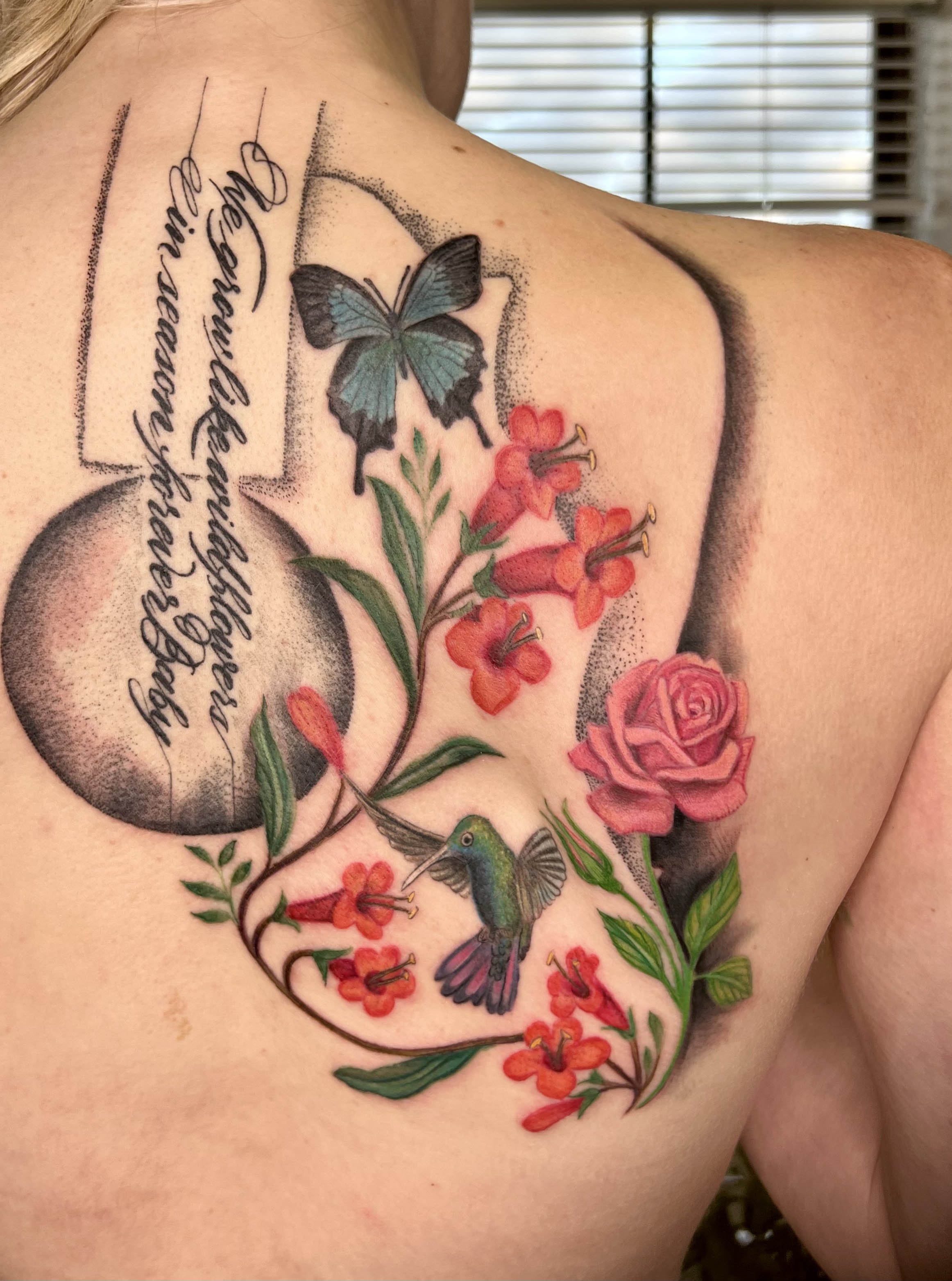  Color tattoo of flowers that make a design on a silhouette of a Gibson guitar with song lyrics on the neck of the guitar.  done on the back of a slender person with pink undertones. Feminine shape.  