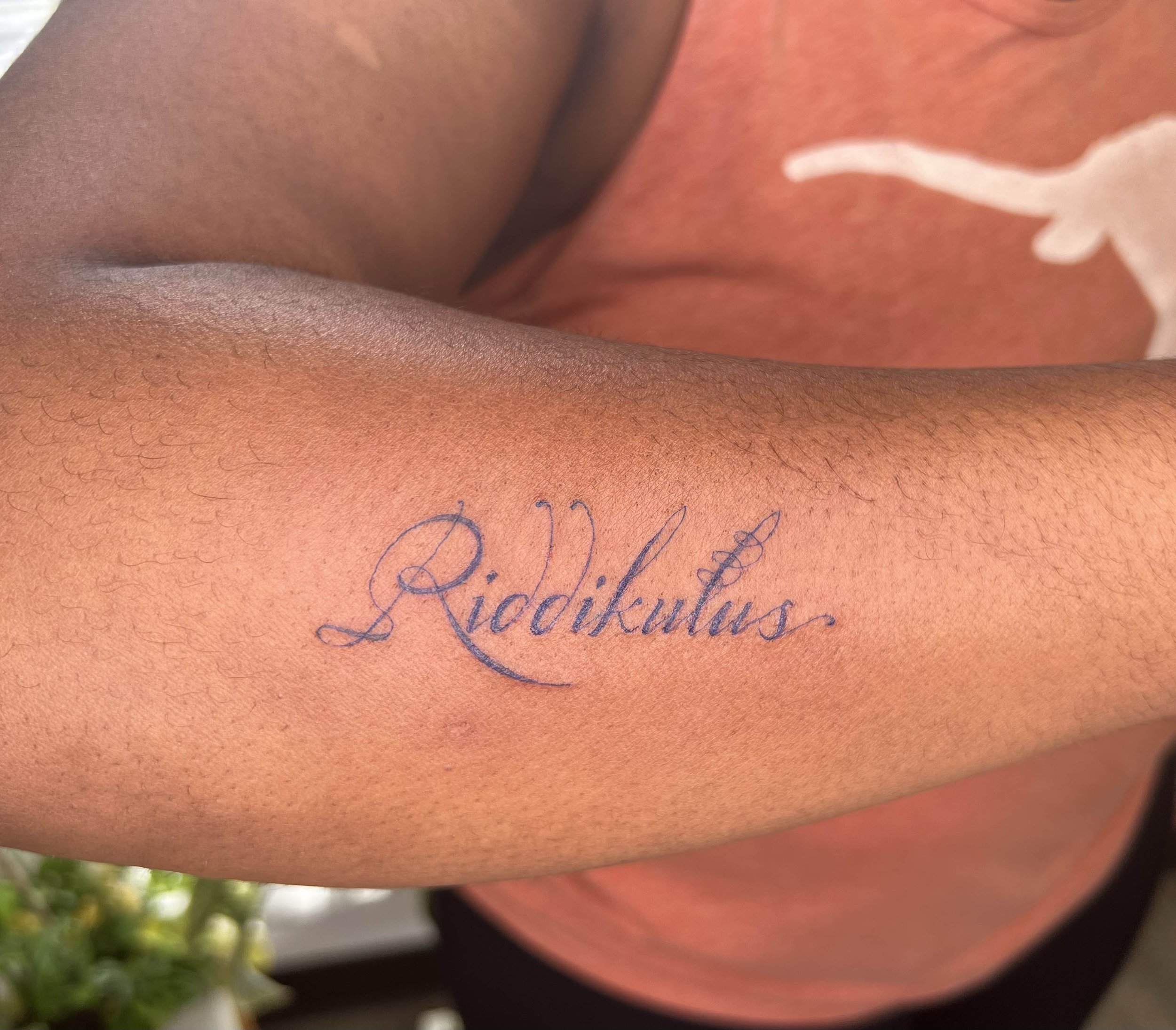  harry potter tattoo old style calligraphy tattoo done in purple on dark skin tone, highly melanated skin tone  