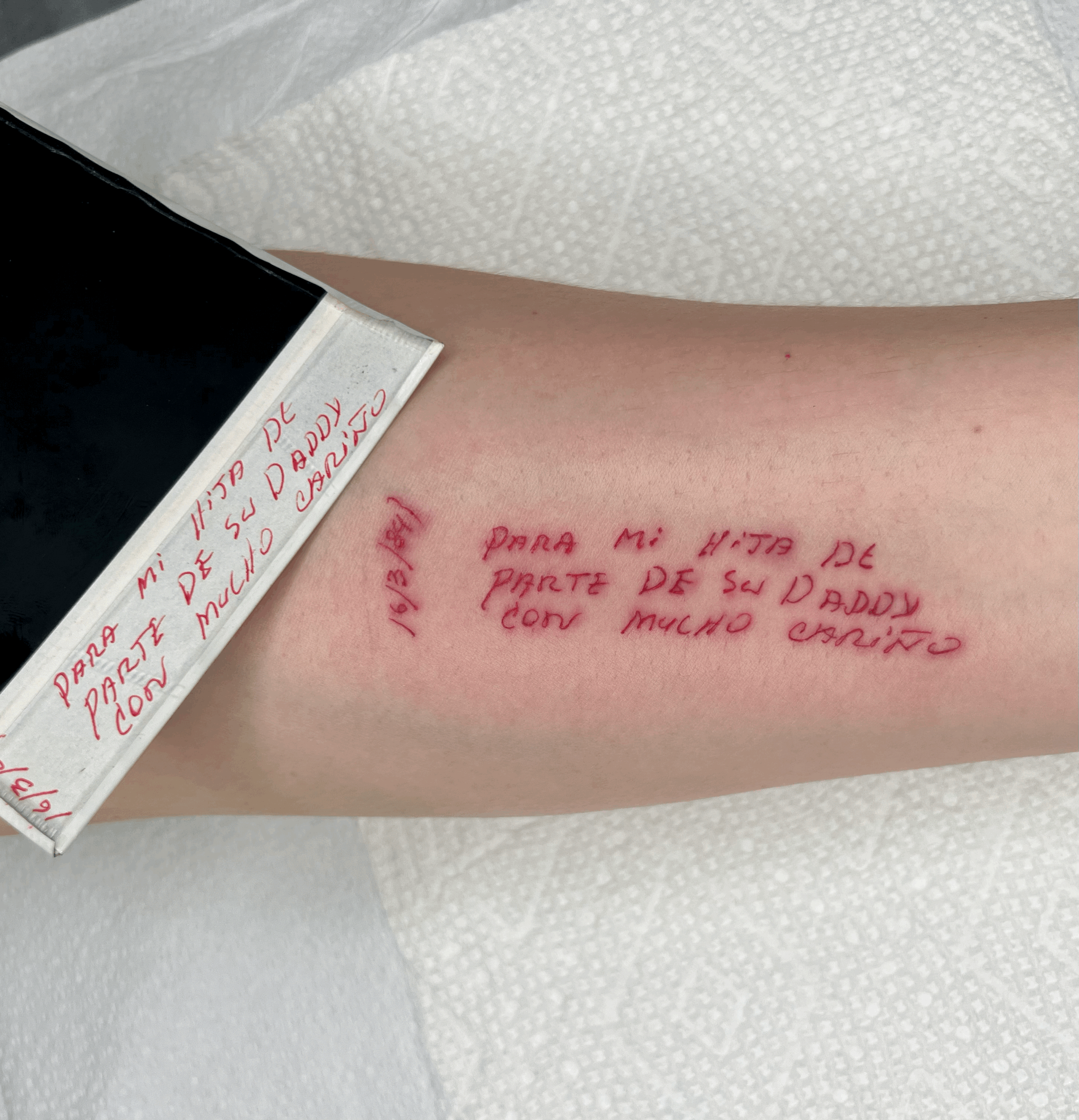  red ink tattoo of Spanish language handwriting from an old polaroid photo. Done on the forearm of a beige skin toned person.  