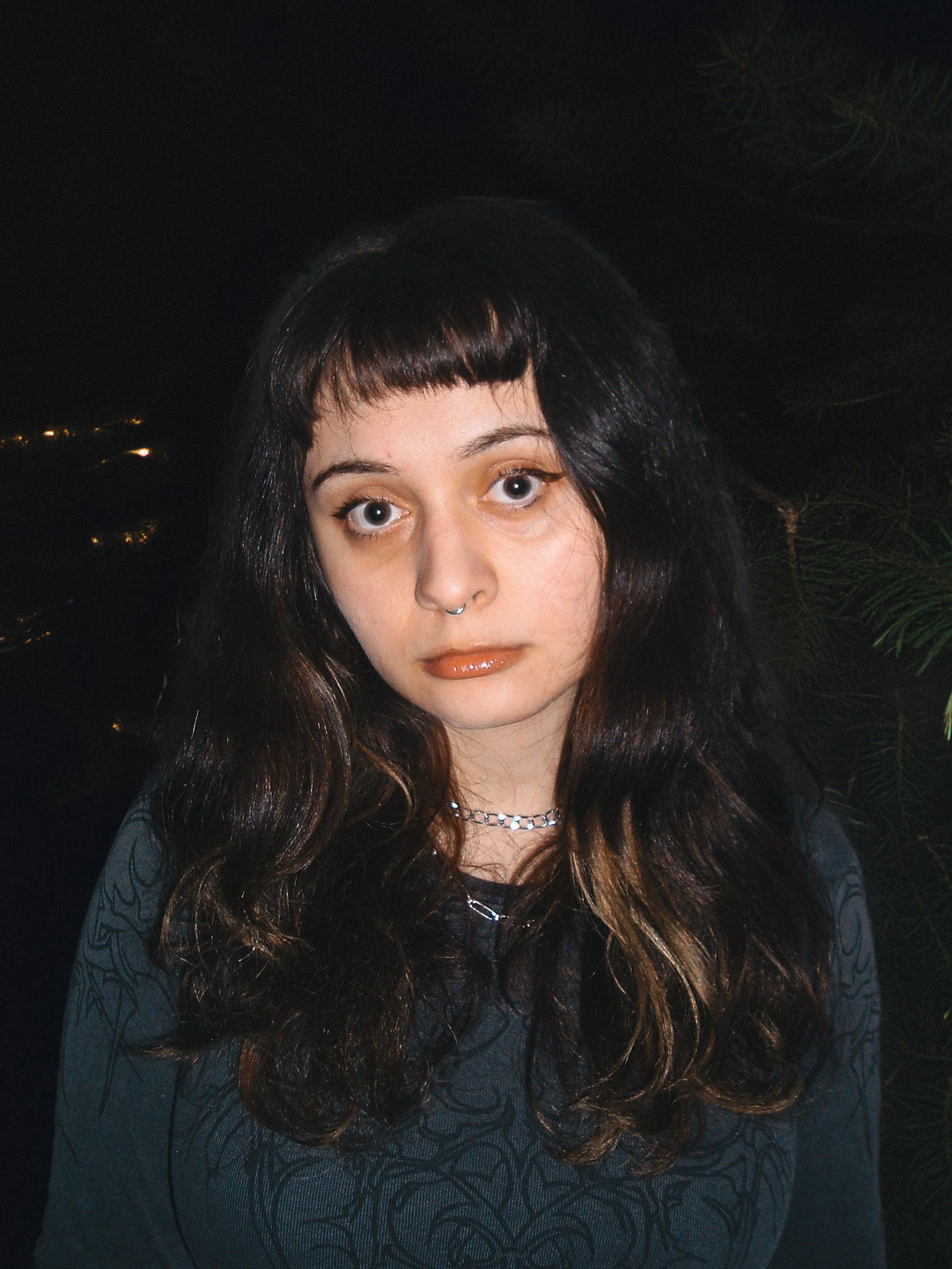 Samantha Locock a feminine presenting person with long brown hair and a grey topposes in front of dark background