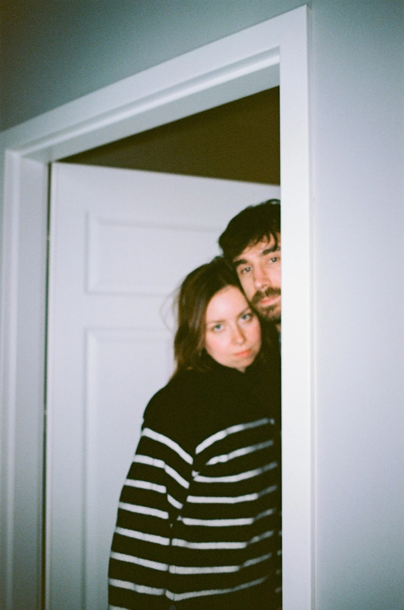 A man and woman peeking out from a partially open door in a close-up shot.