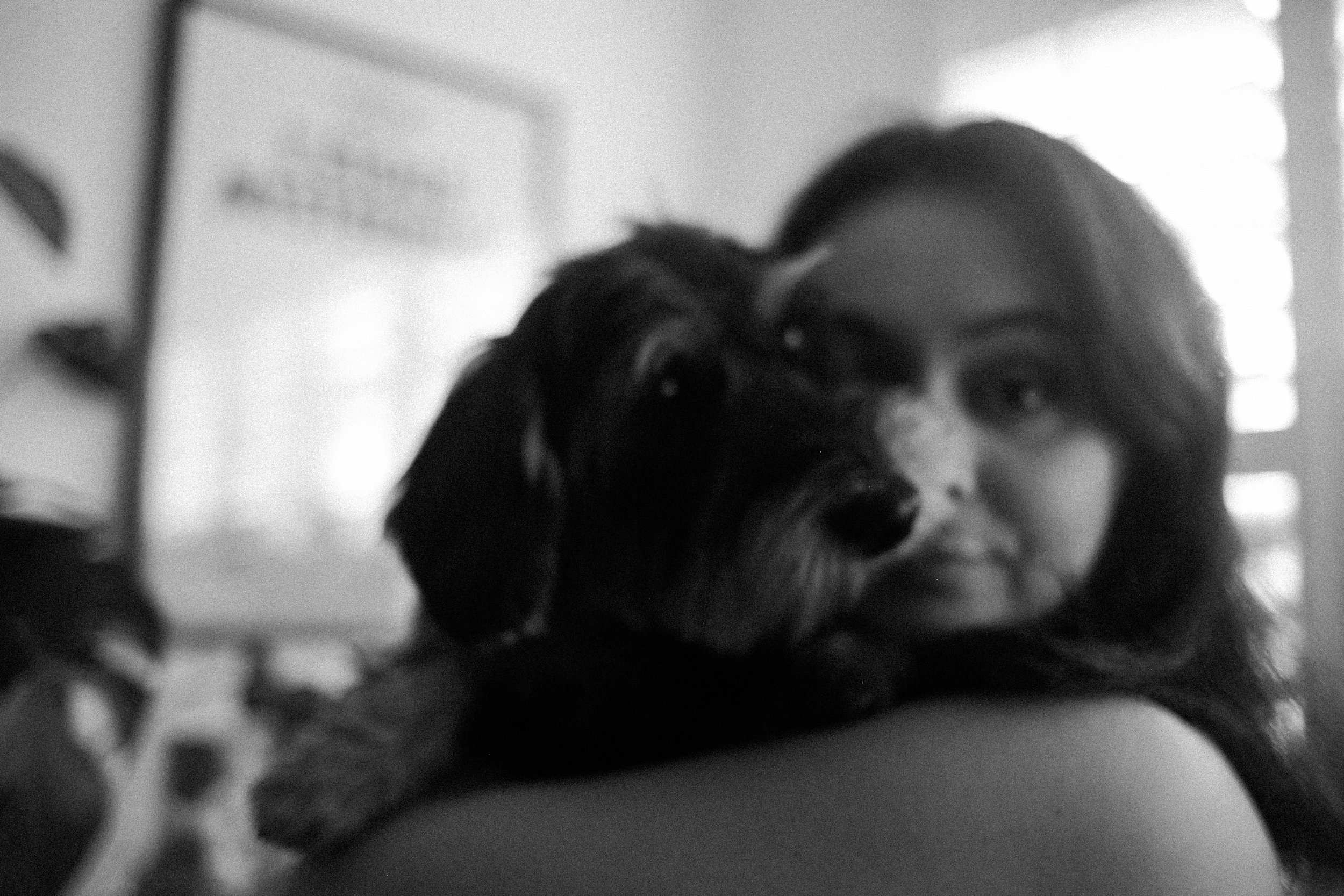 A woman with long hair holding a small dog close to her face, both looking at the camera, in black and white.