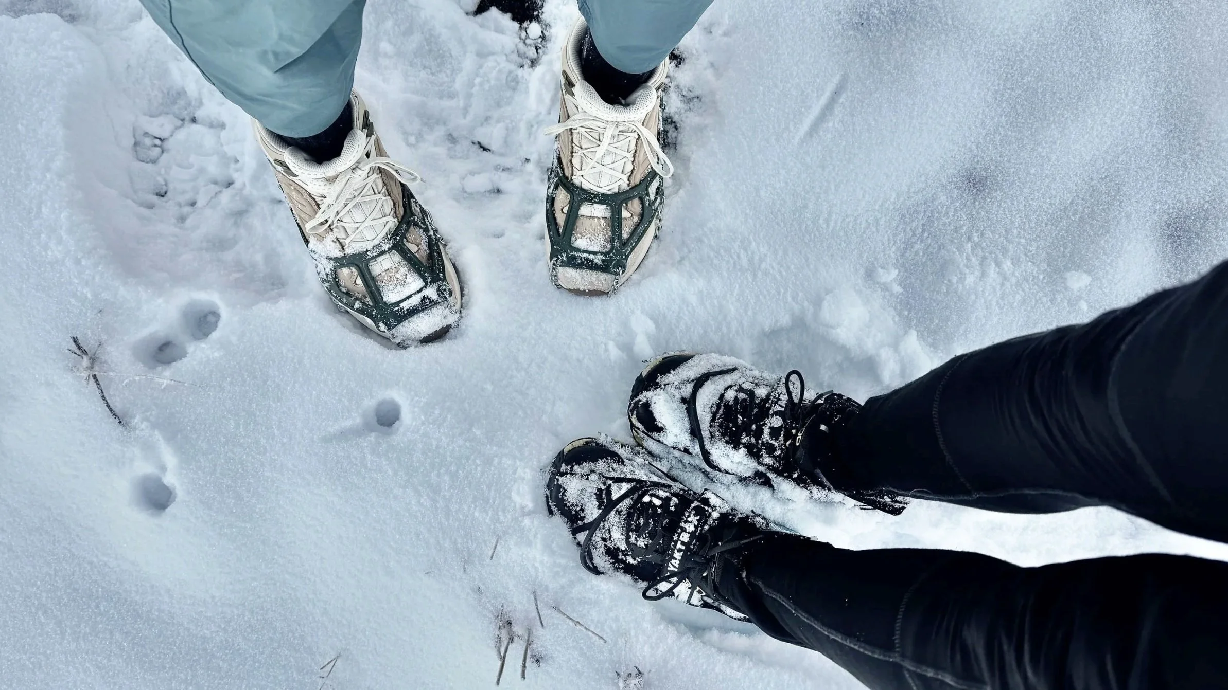 Two hikers wearing traction cleats on a snow-covered mountain trail near Bozeman, Montana.