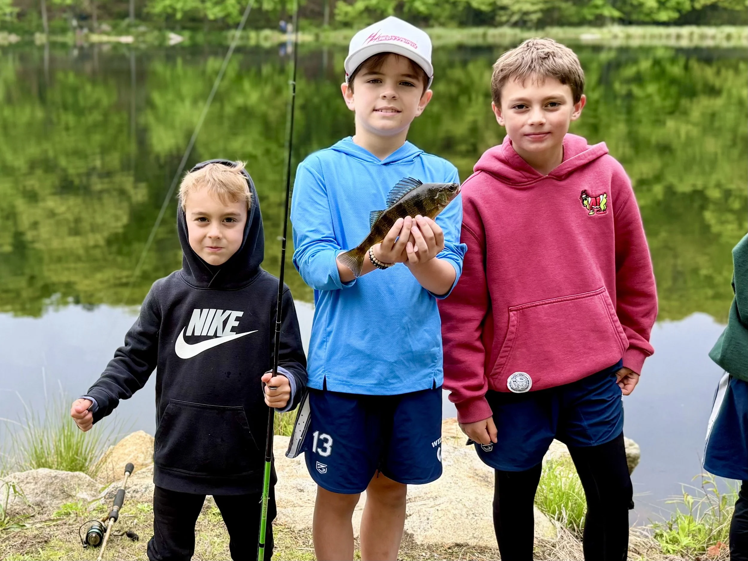 Three young boys fishing. One holds up a fish.